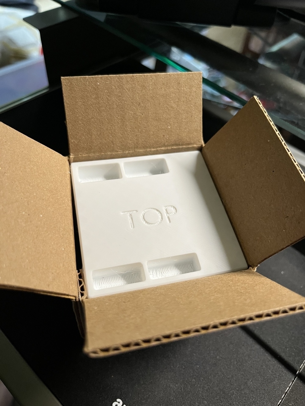 An open cardboard box contains a white plastic insert labeled TOP.