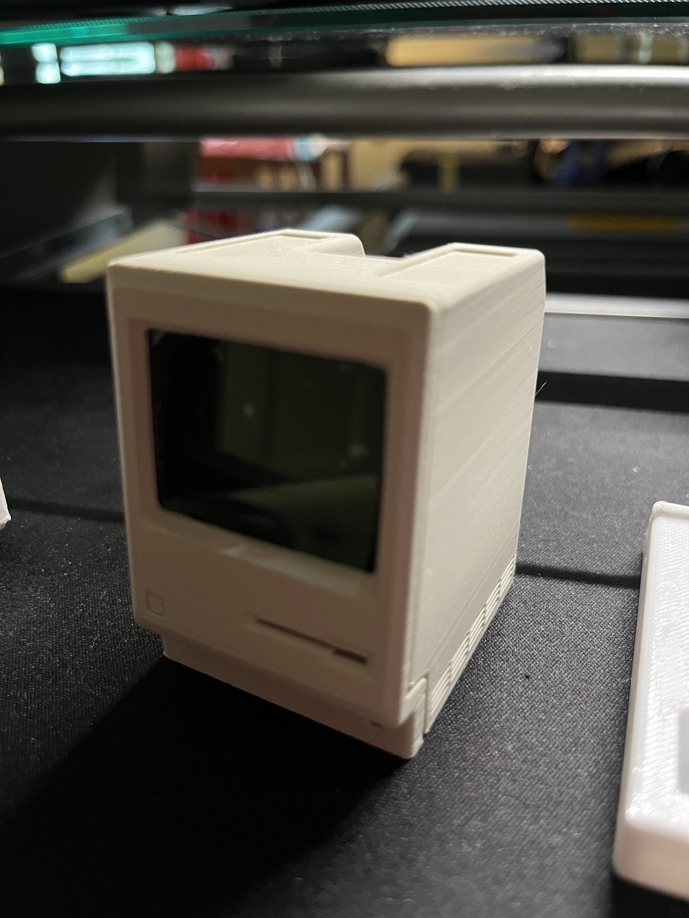A small, vintage-style computer with a CRT display and a floppy disk slot is shown on a dark surface.