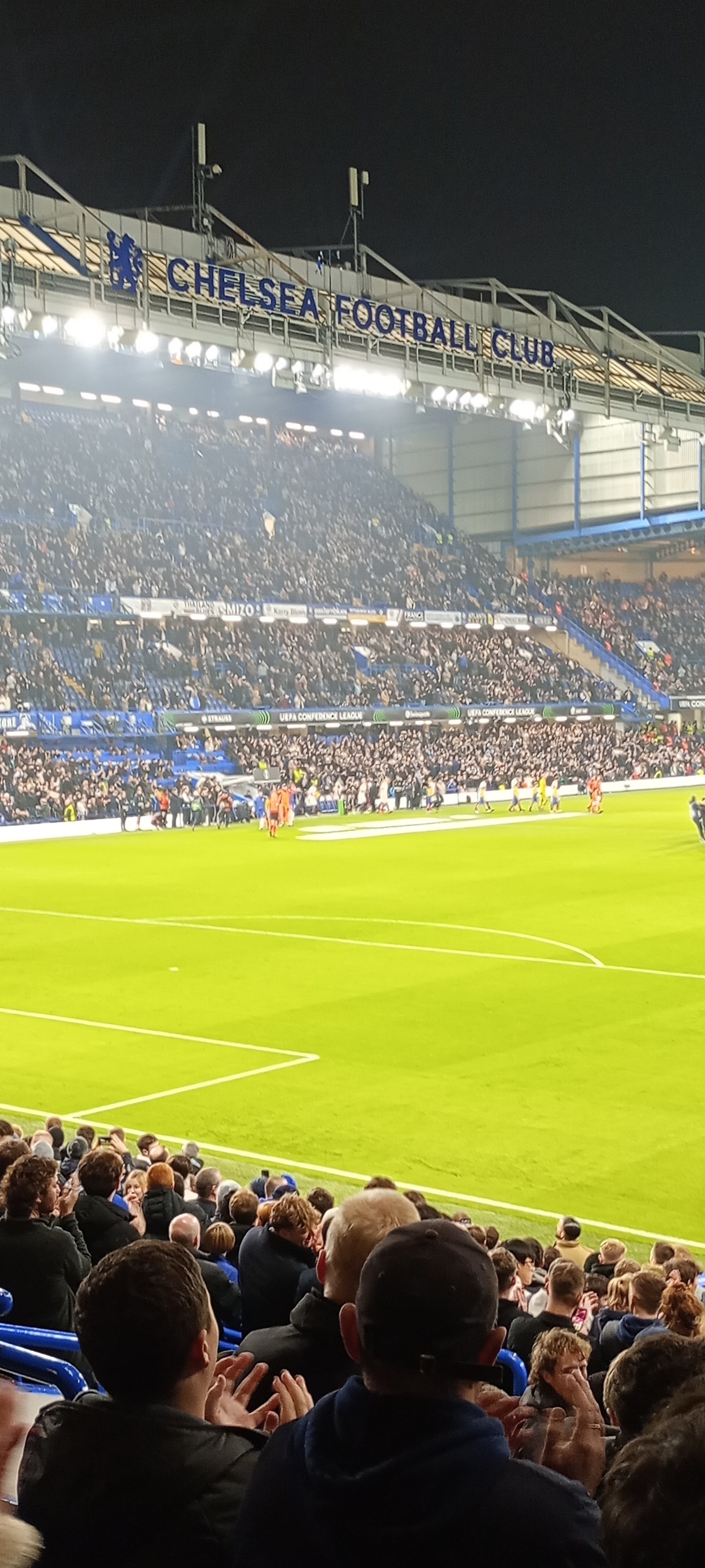 A football match is taking place at Chelsea's Stamford Bridge stadium, with a packed crowd in attendance.