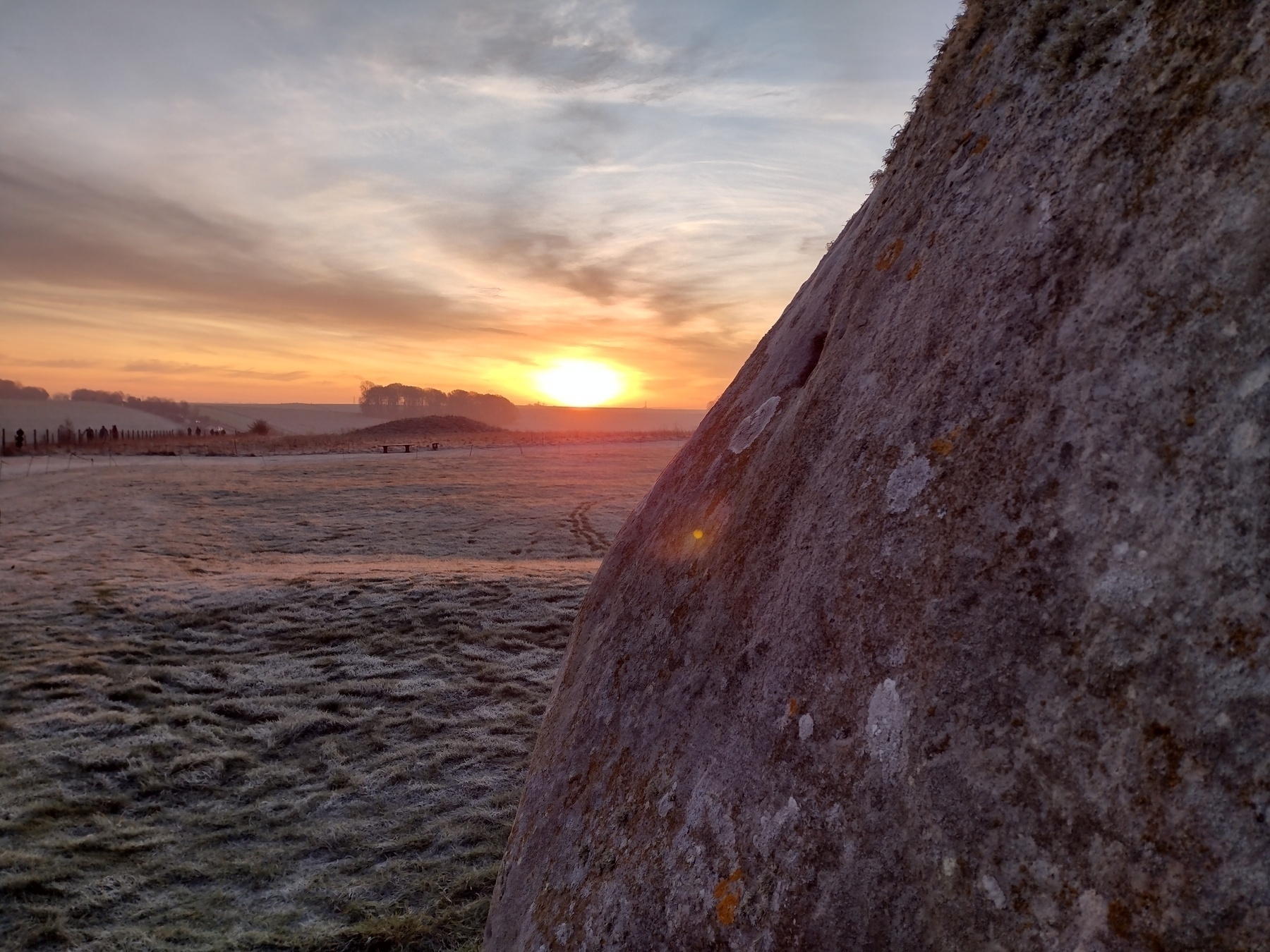 A large stone stands in the foreground against a frosty landscape at sunrise.