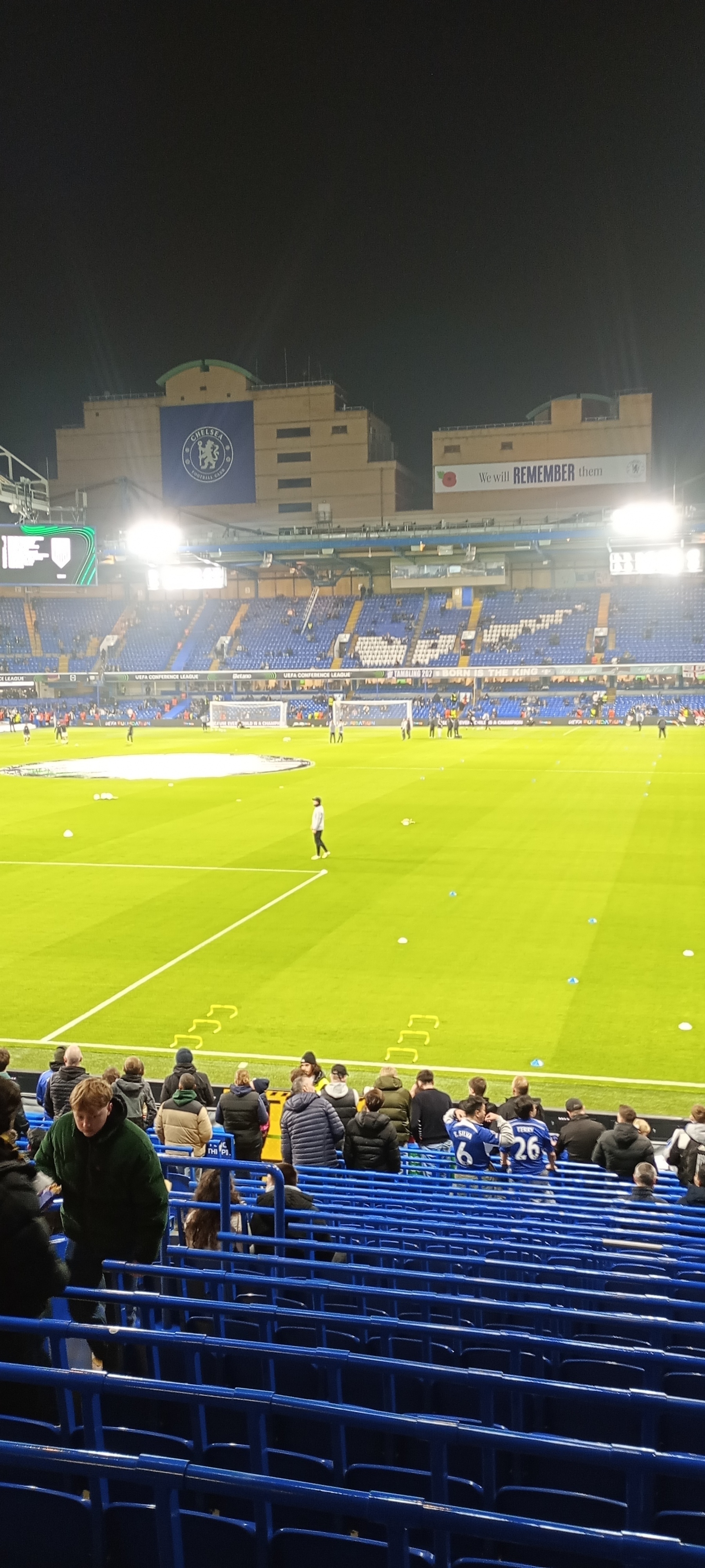 A soccer stadium is shown with people in the stands and players on the field under bright lights.