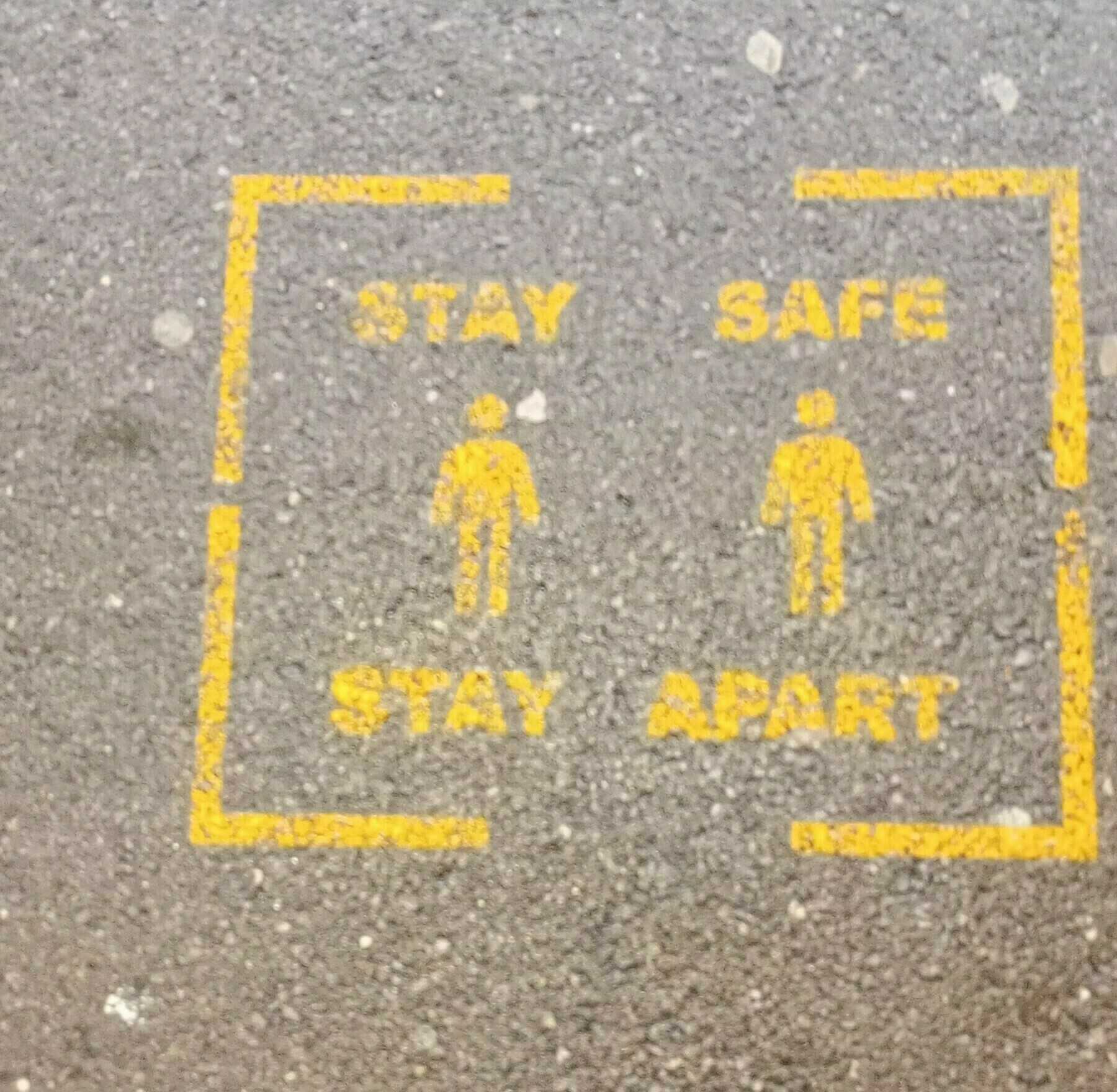 A pavement marking displays figures and the message Stay Safe Stay Apart to encourage social distancing.