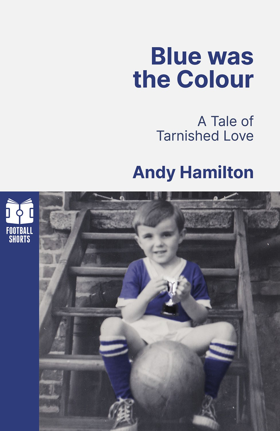 Auto-generated description: A young child wearing a blue football uniform sits on stairs holding a trophy, with a football at their feet, next to the book title Blue was the Colour: A Tale of Tarnished Love by Andy Hamilton.