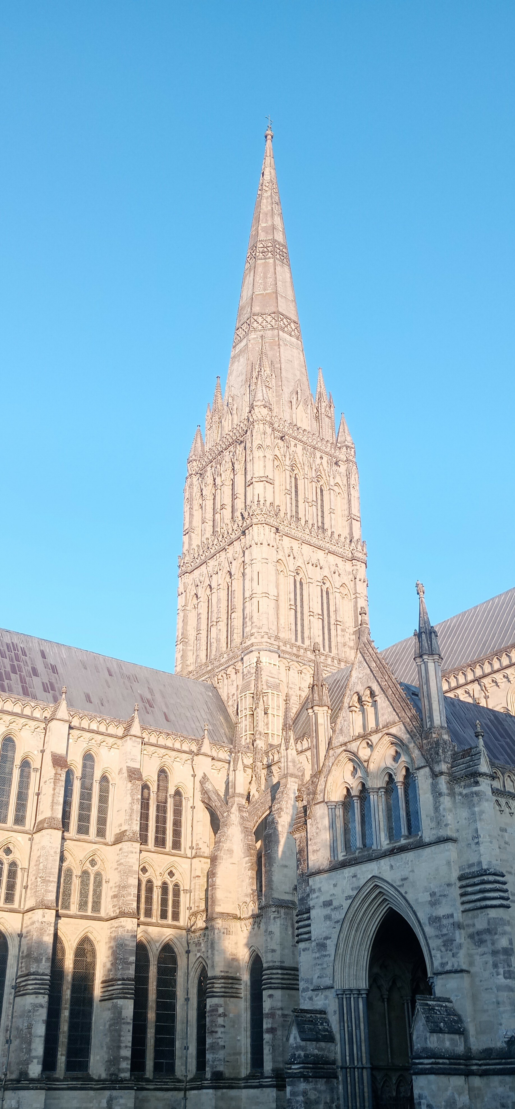 A large Gothic cathedral with a tall spire is set against a clear blue sky.
