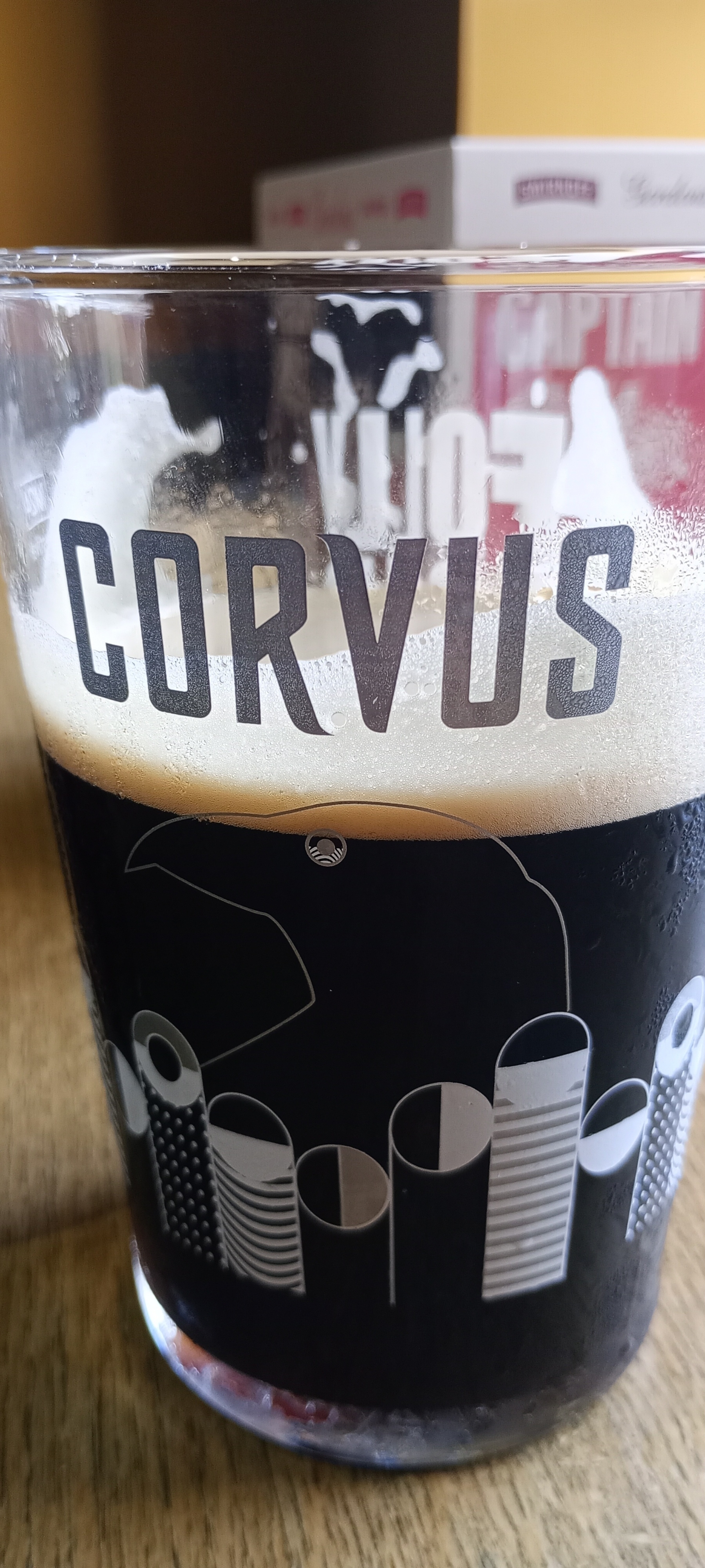 A glass filled with dark beer features the word "CORVUS" and a stylized graphic design.