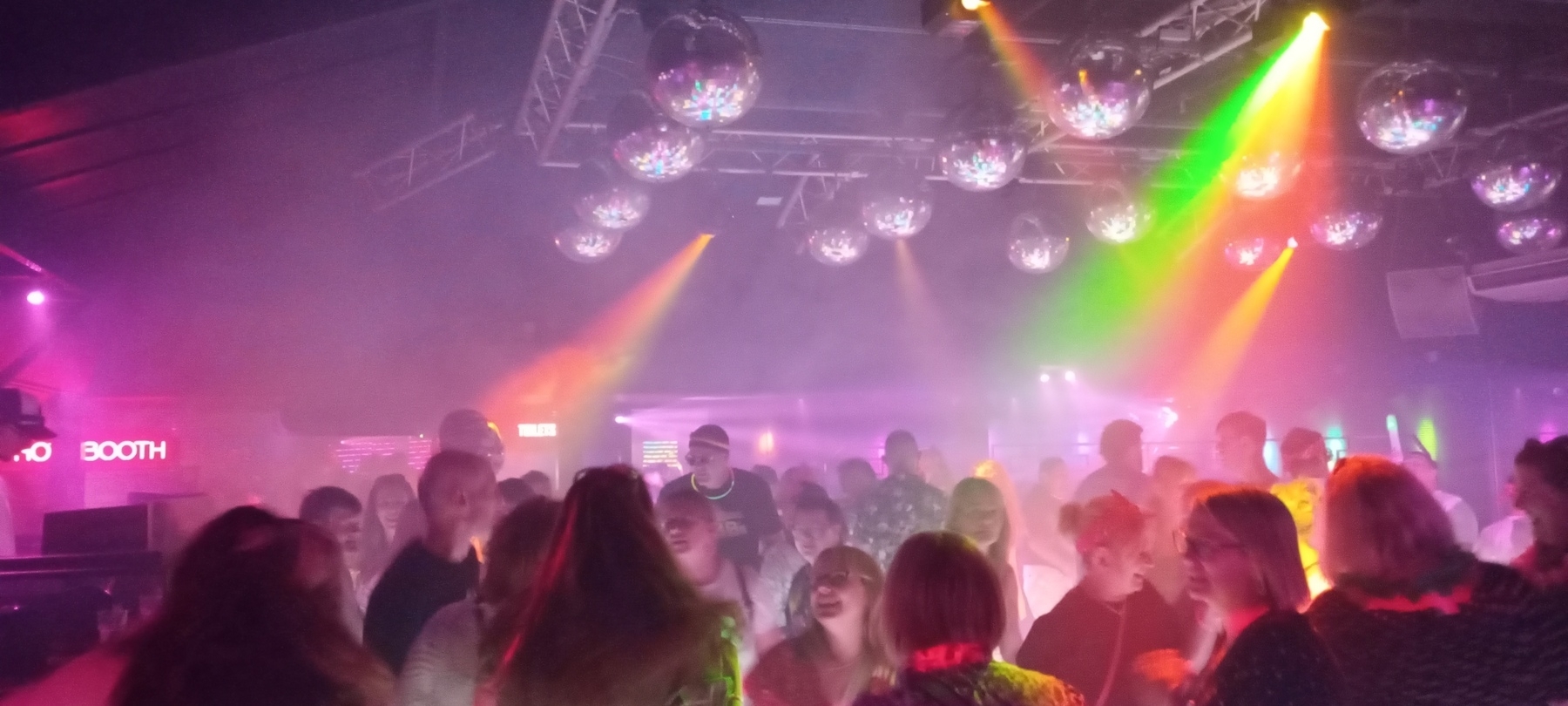 A lively nightclub scene with colorful lighting, disco balls, and a crowd of people dancing.