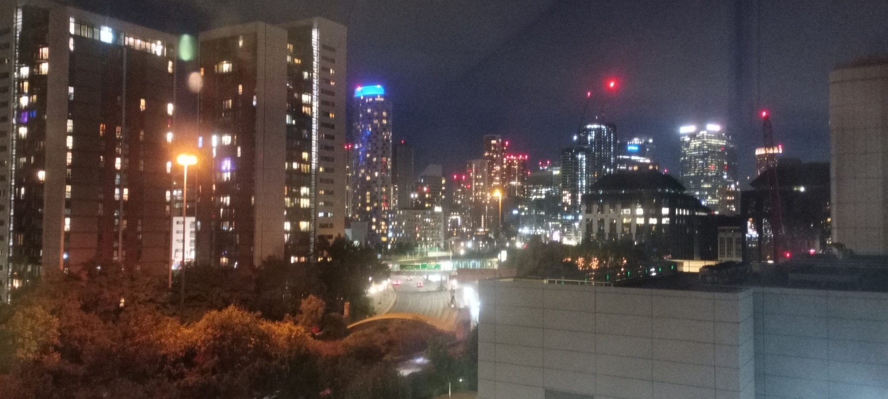 Auto-generated description: A city skyline is illuminated at night with numerous brightly lit buildings and red lights atop towers.