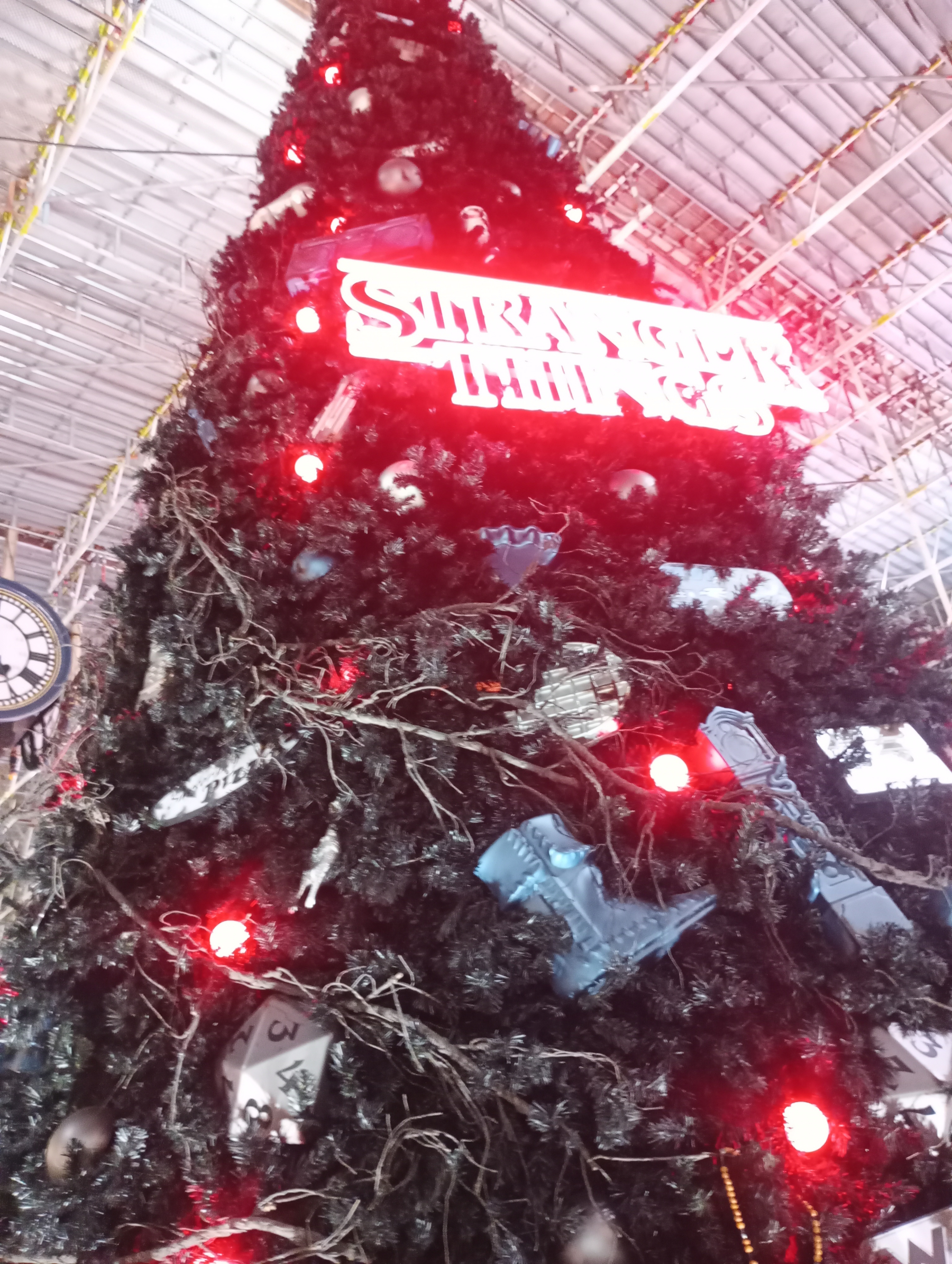 A large, black Christmas tree is adorned with red lights and various decorations under a glowing sign.