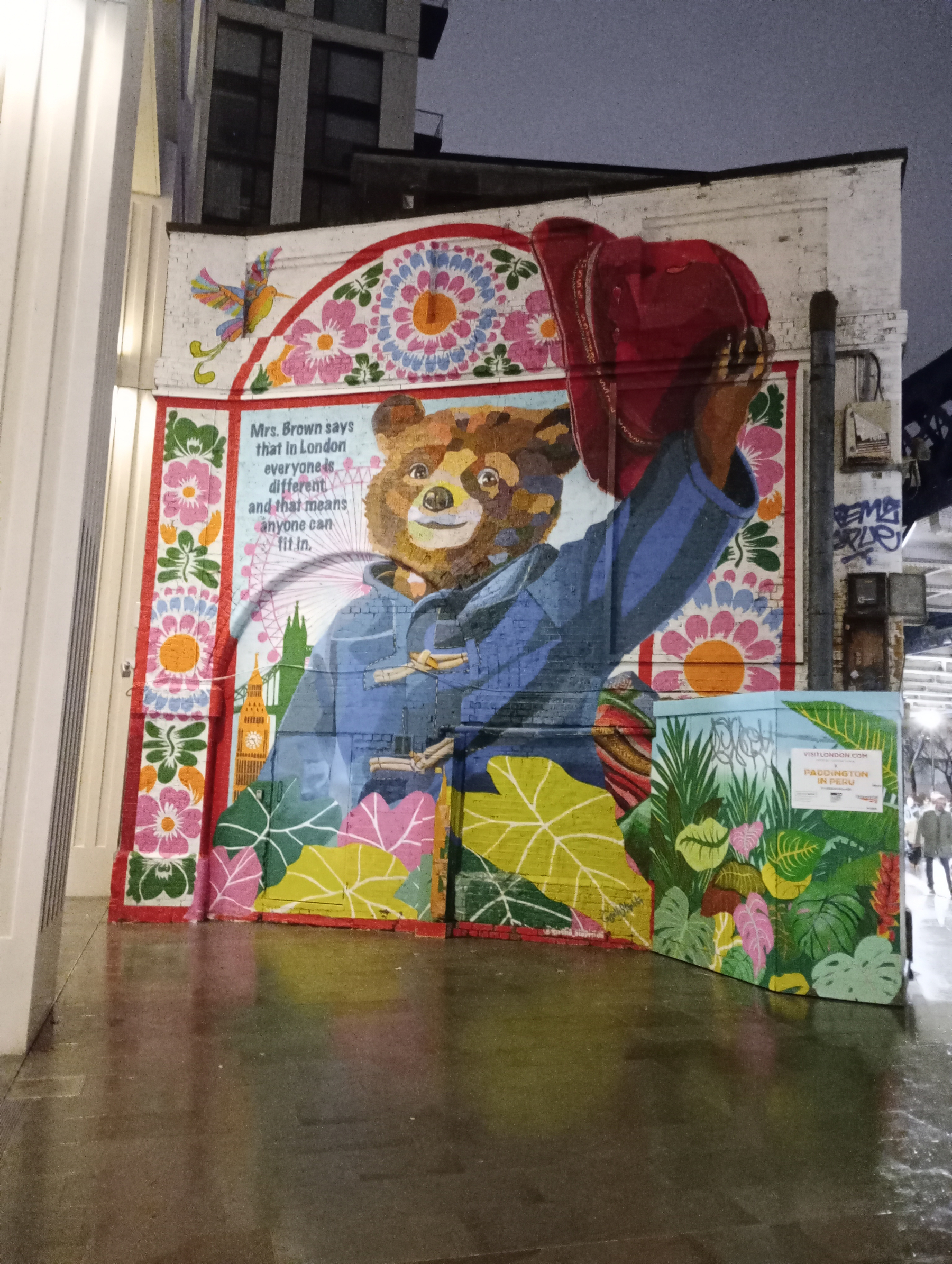 A vibrant mural of a bear in a blue coat holding a red hat, surrounded by colorful flowers and patterns, adorns the wall.