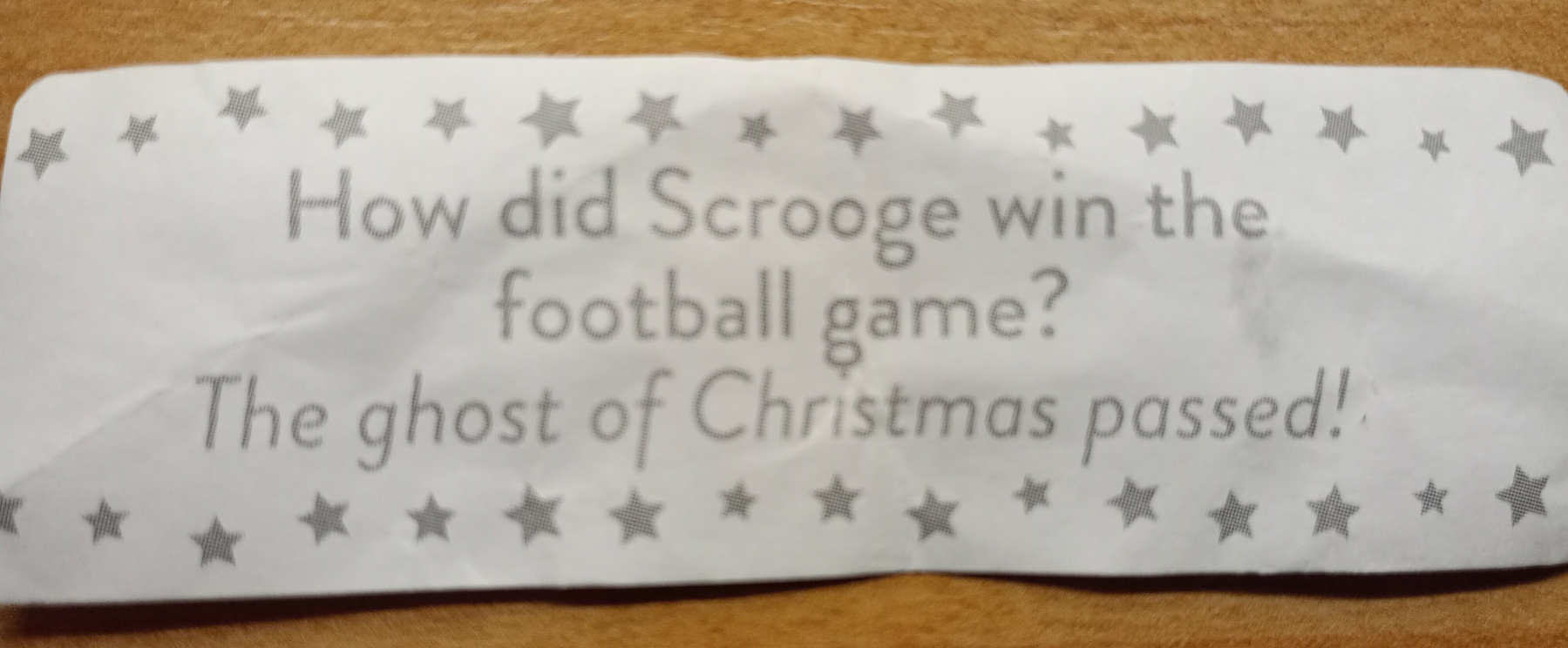 A fortune cookie paper containing a joke that asks, How did Scrooge win the football game? with the punchline, The ghost of Christmas passed!