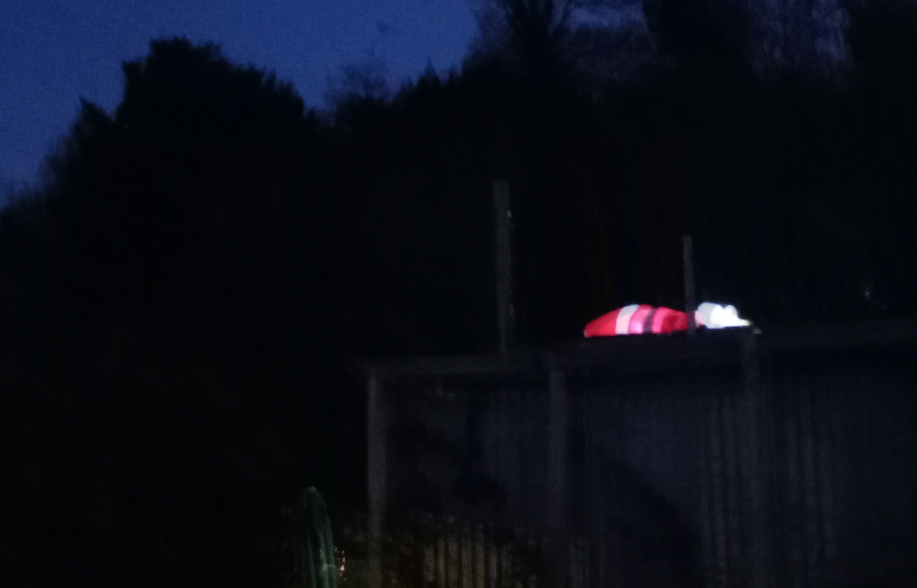 A dimly lit outdoor scene features a structure with what appears to be illuminated holiday decorations resembling a Santa figure on top.