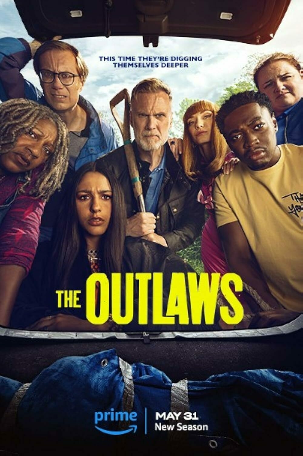 A group of seven diverse individuals, some holding tools, are gathered around a large blue bag, featured on a poster for "The Outlaws" 