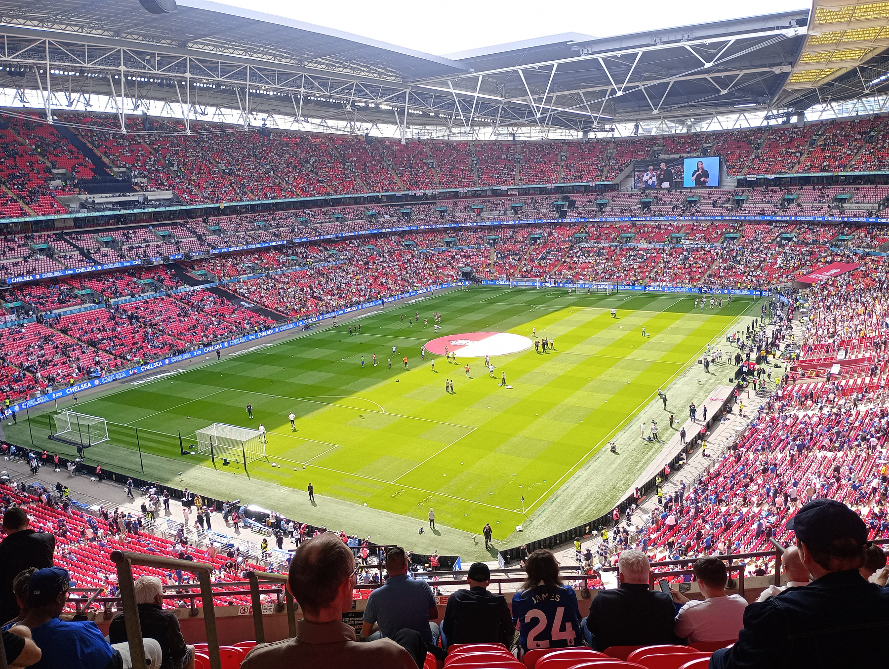 A large football stadium filled with spectators showcases teams warming up on the field before a match.