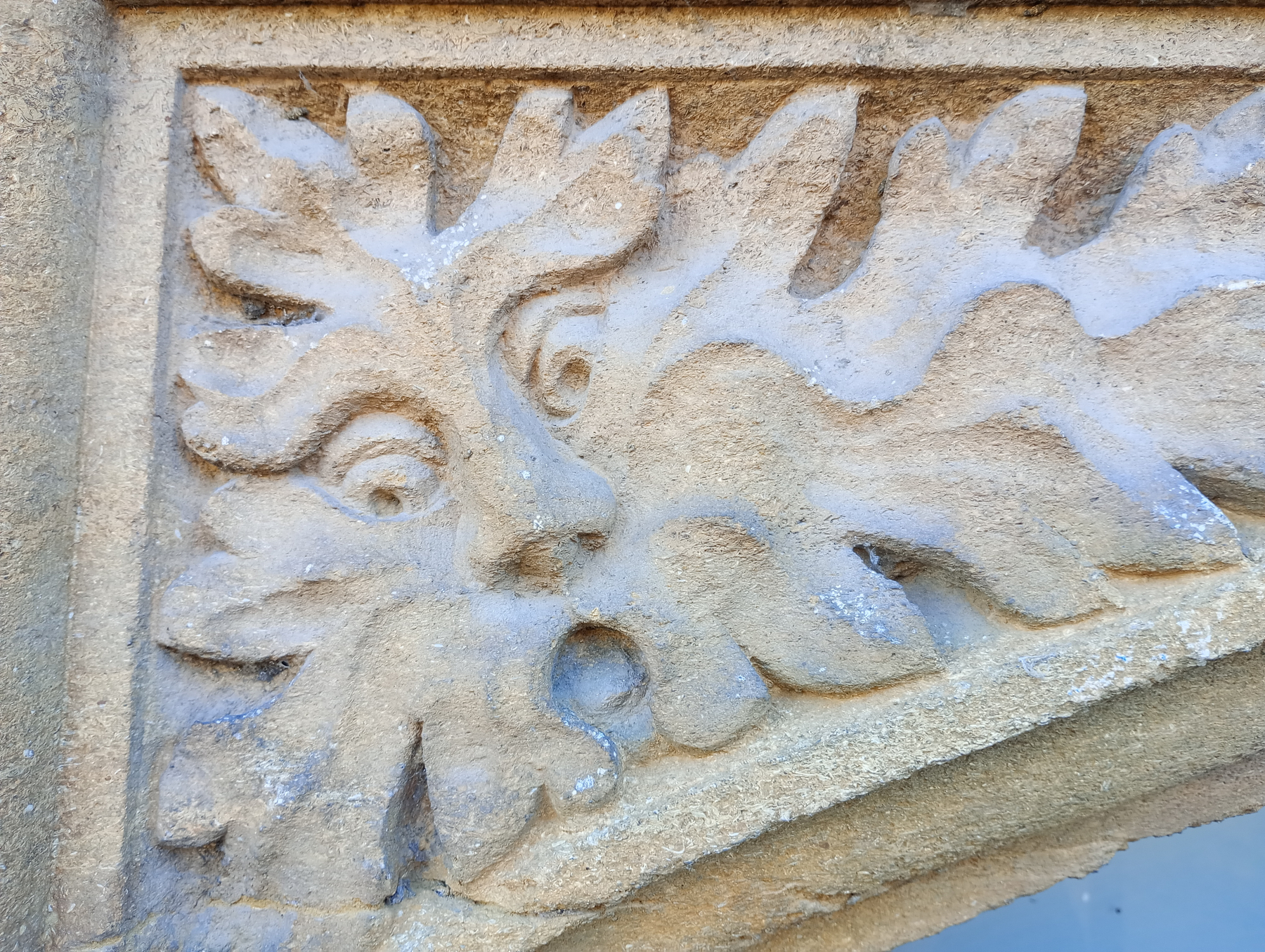 An intricate stone carving features a stylized face with leaf-like extensions.