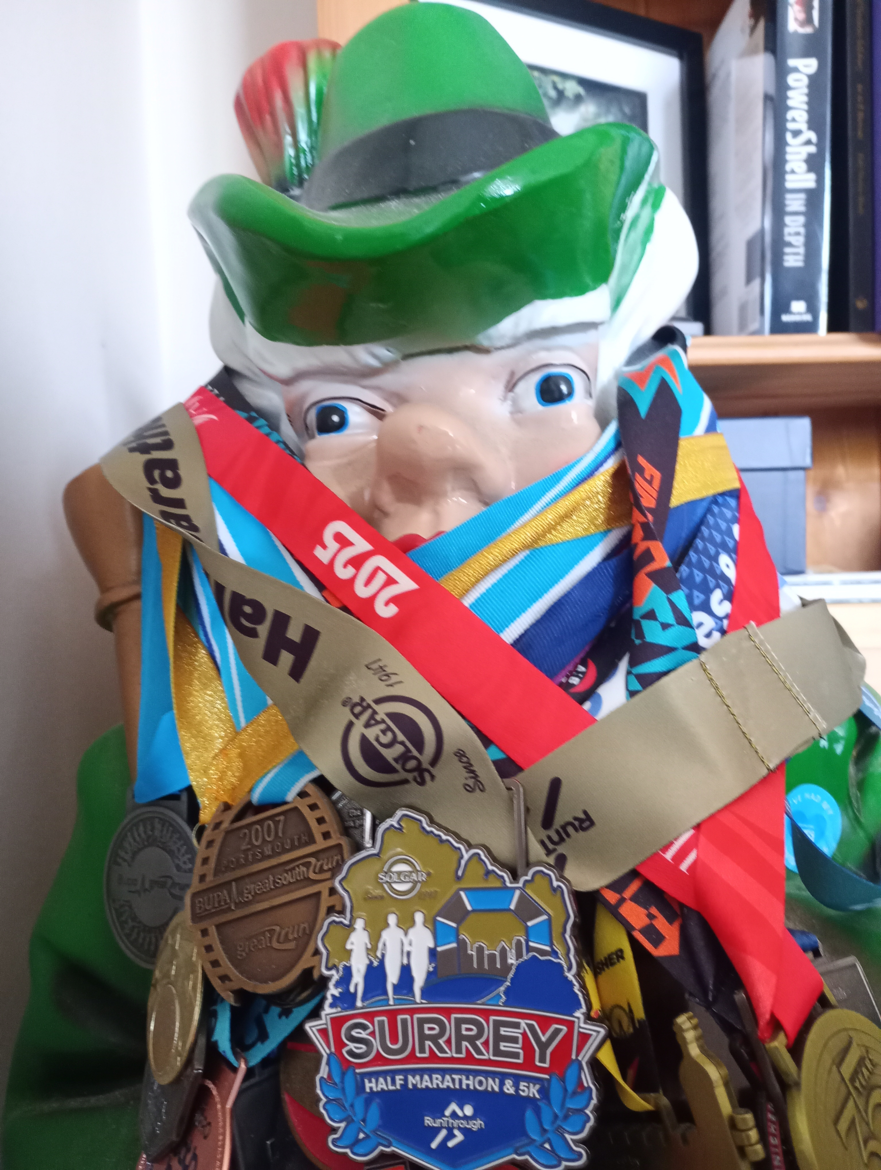 A statue of a leprechaun is adorned with numerous colorful race medals, including one prominently featuring Surrey Half Marathon & 5K.