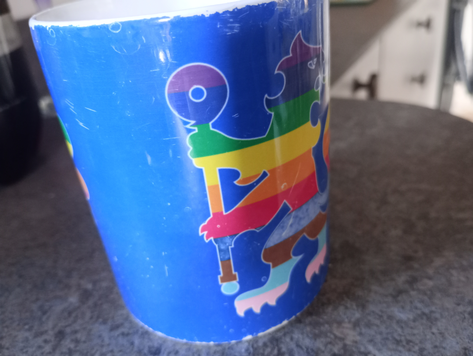A colorful, abstract design featuring a figure holding a device adorns a blue mug placed on a countertop.