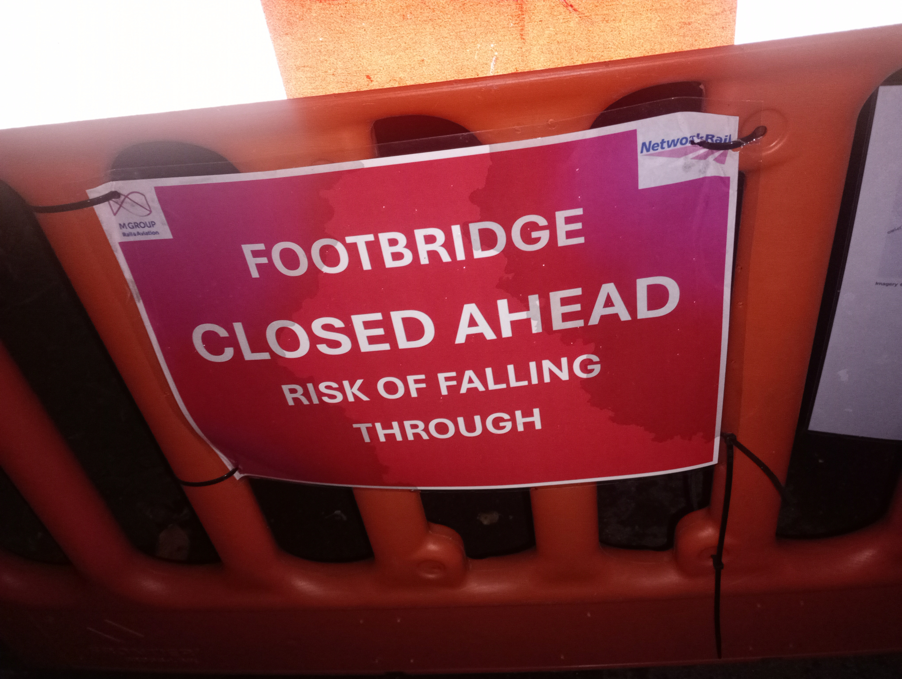 A warning sign indicates that the footbridge ahead is closed due to the risk of falling through.