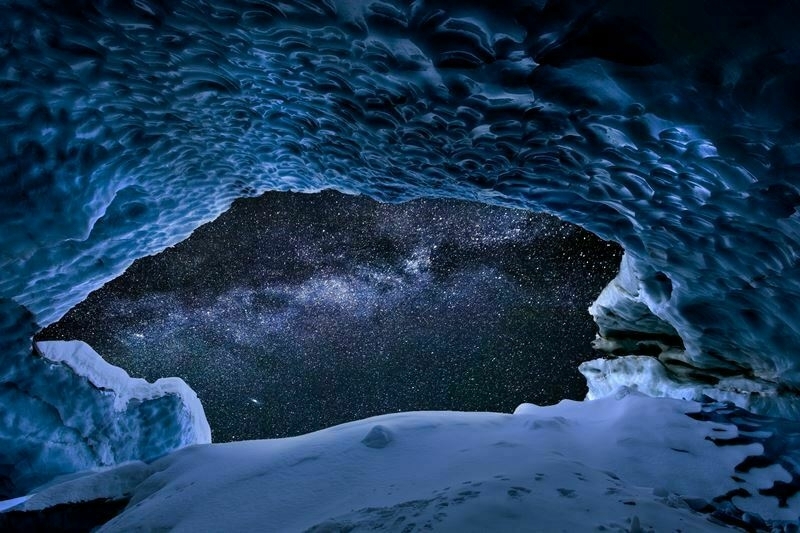 The view from inside an ice cave, looking out at a starry night sky.