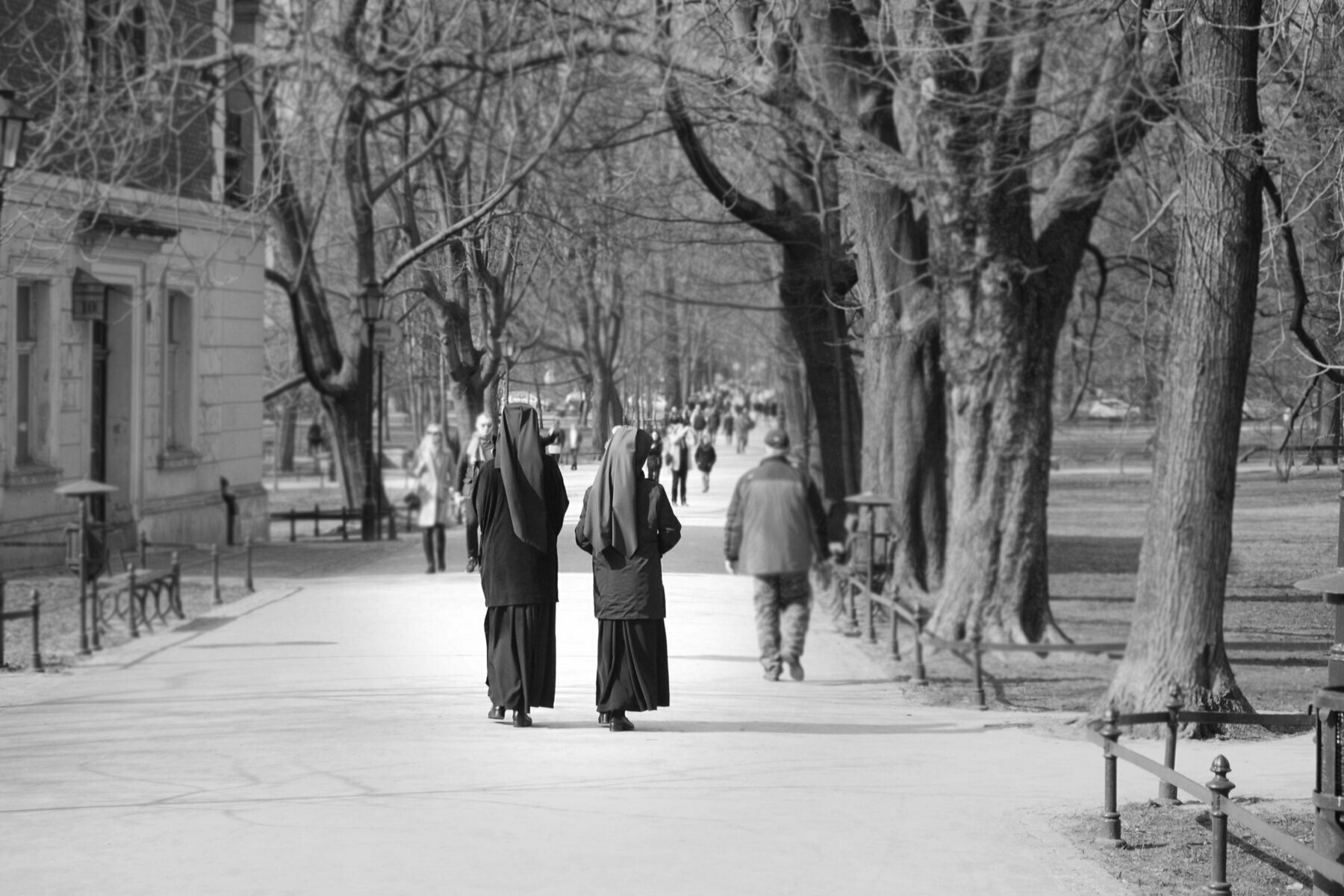 A black and white photograph of two nuns walking next to some trees