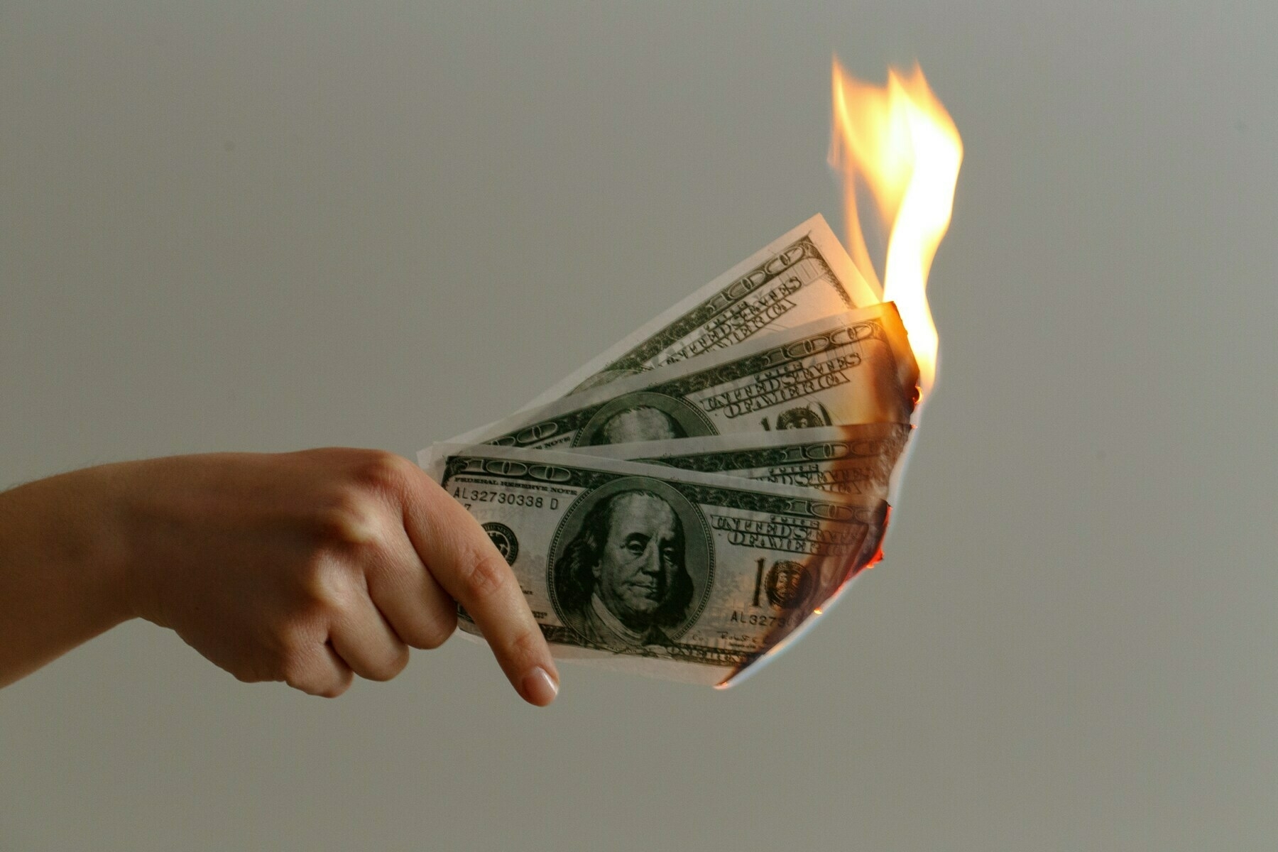 Hand holding several $100 bills on fire