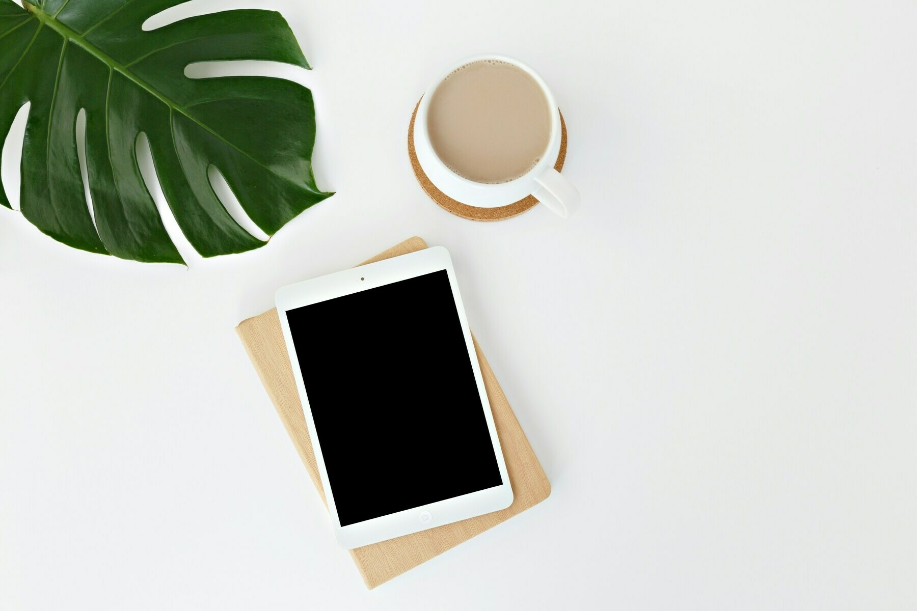 iPad, coffee, and leaf on a white surface