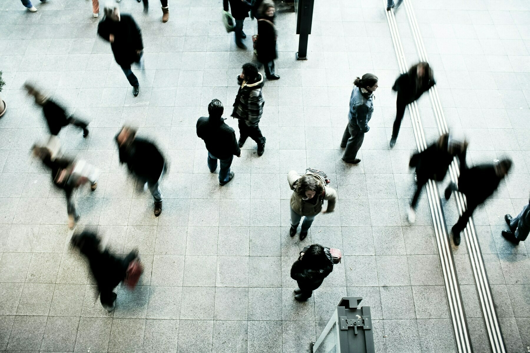 Overhead view of a busy indoor area with blurred figures walking, capturing the motion and activity of a crowded public space.