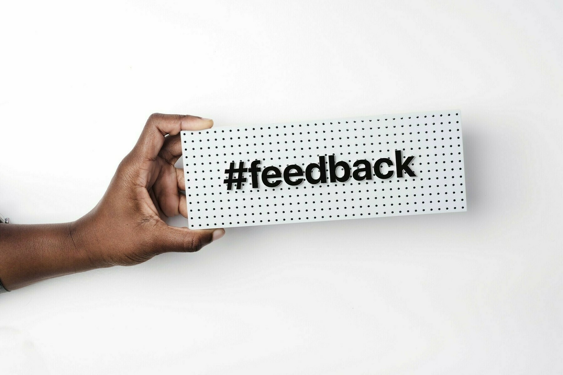 Auto-generated description: A hand is holding a perforated board with the word #feedback on it.