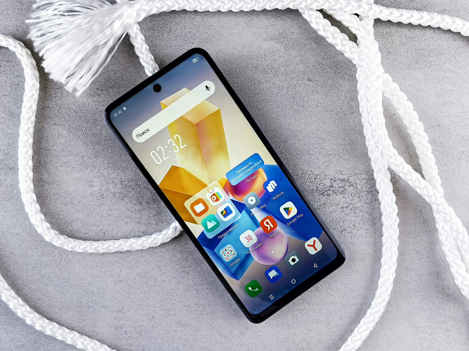 Auto-generated description: A smartphone with a colorful home screen lies on a textured gray surface surrounded by white ropes.