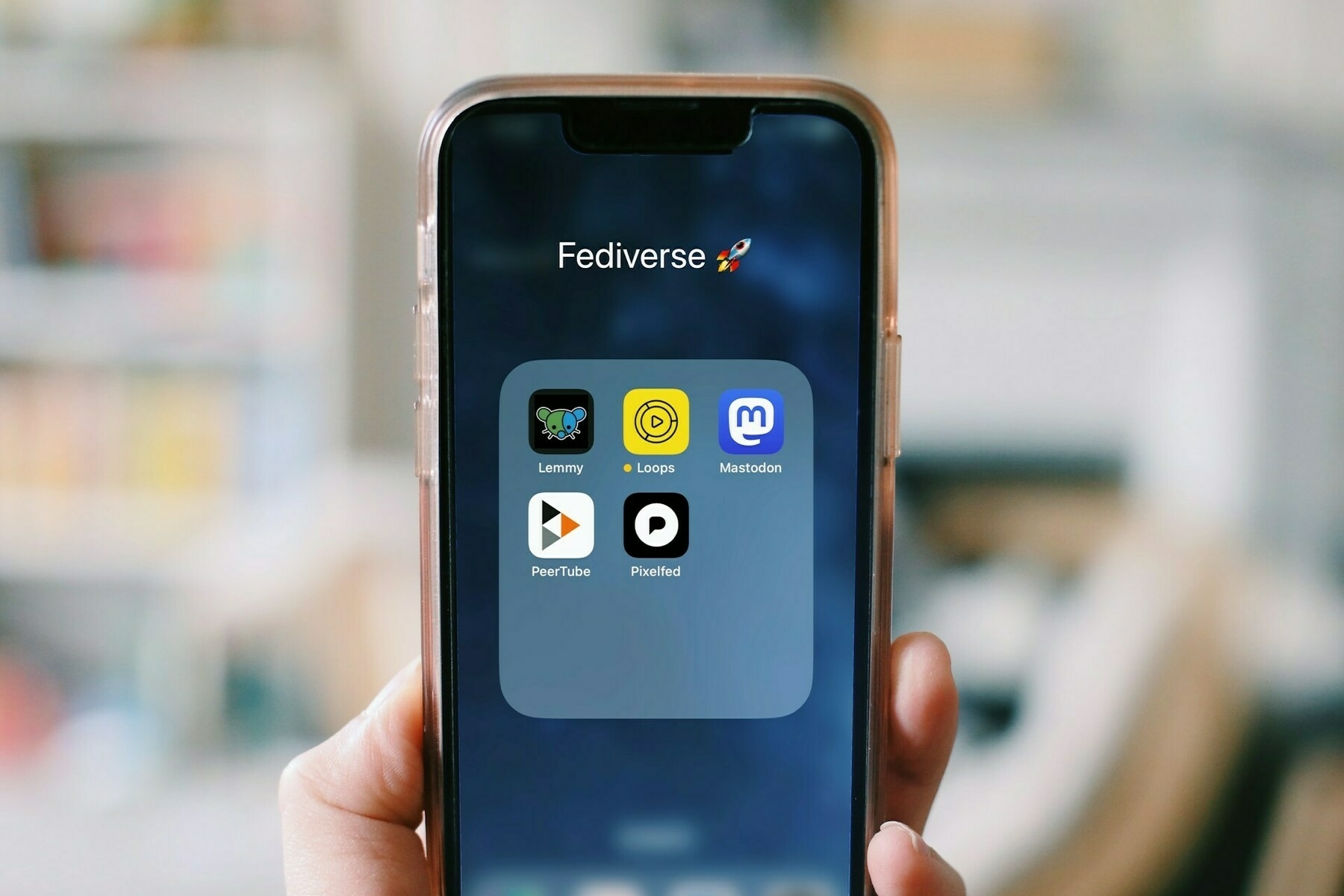 A hand holding a smartphone. The screen shows a folder of Fediverse apps.