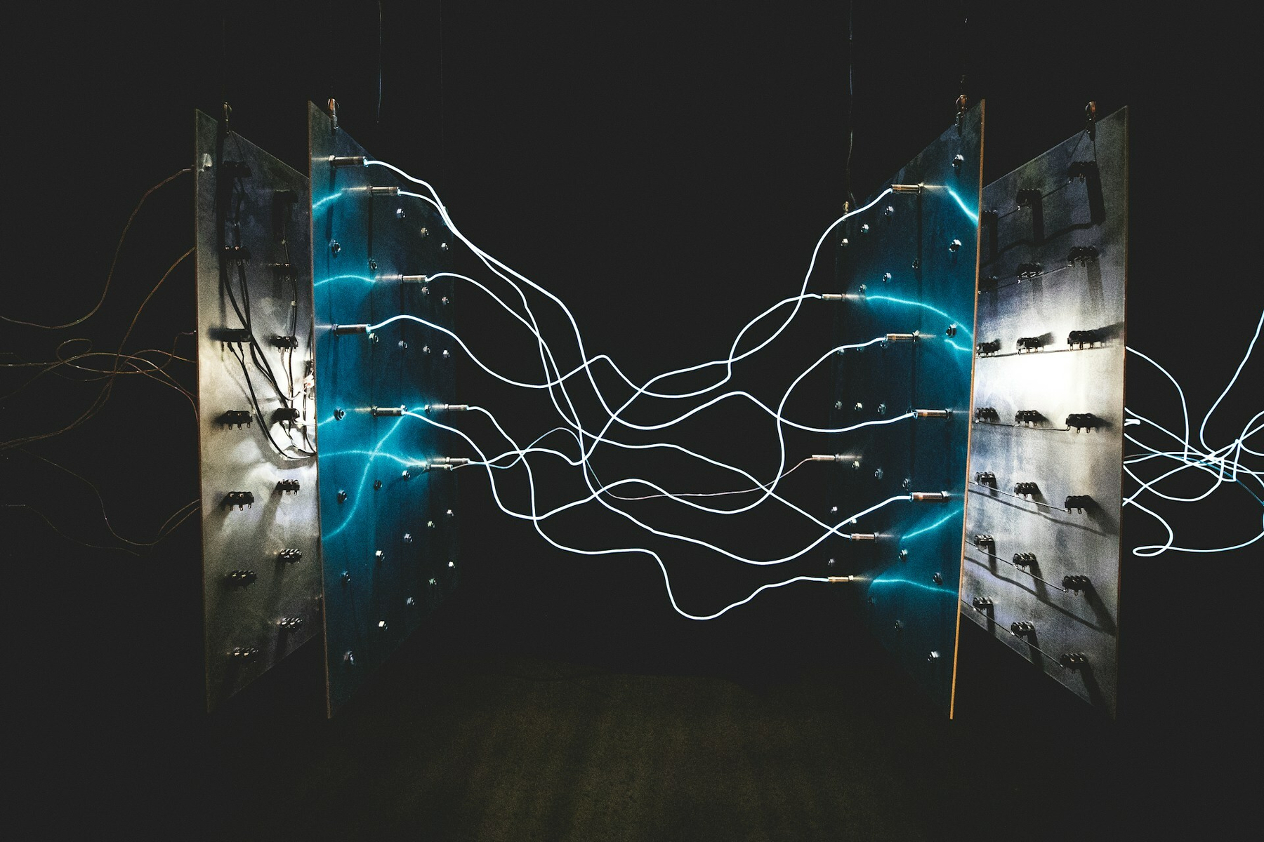 Auto-generated description: Two vertical panels connected by glowing, intertwined wires or cables in a dark setting.