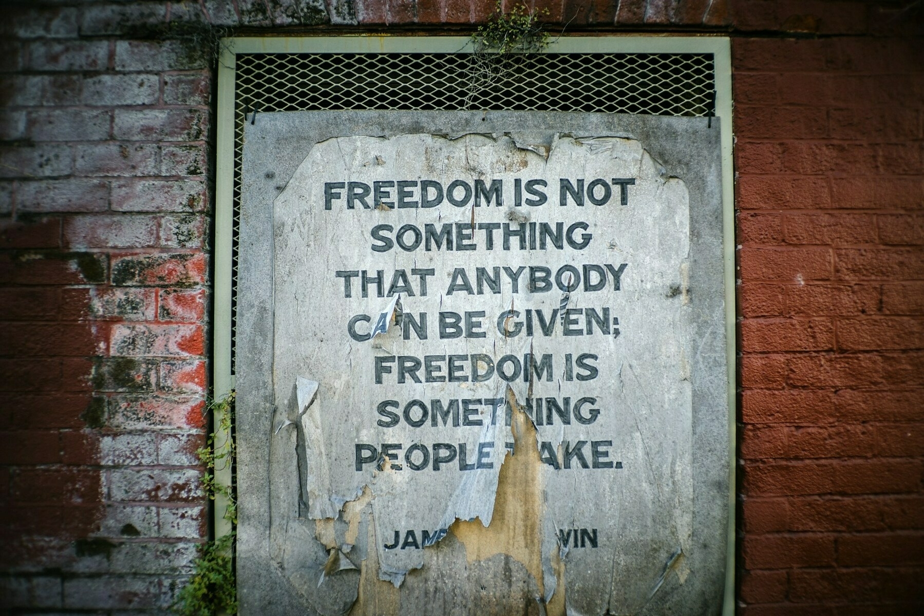 Auto-generated description: A weathered poster on a brick wall displays the quote, Freedom is not something that anybody can be given; freedom is something people take, attributed to James Baldwin.