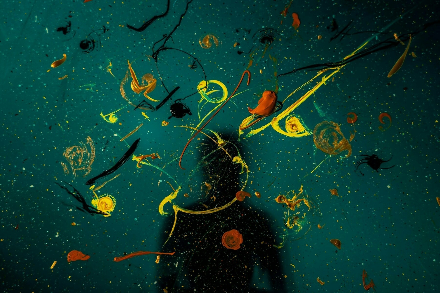 Auto-generated description: A silhouette is visible against a dark backdrop with splatters of bright orange and yellow paint creating an abstract design.