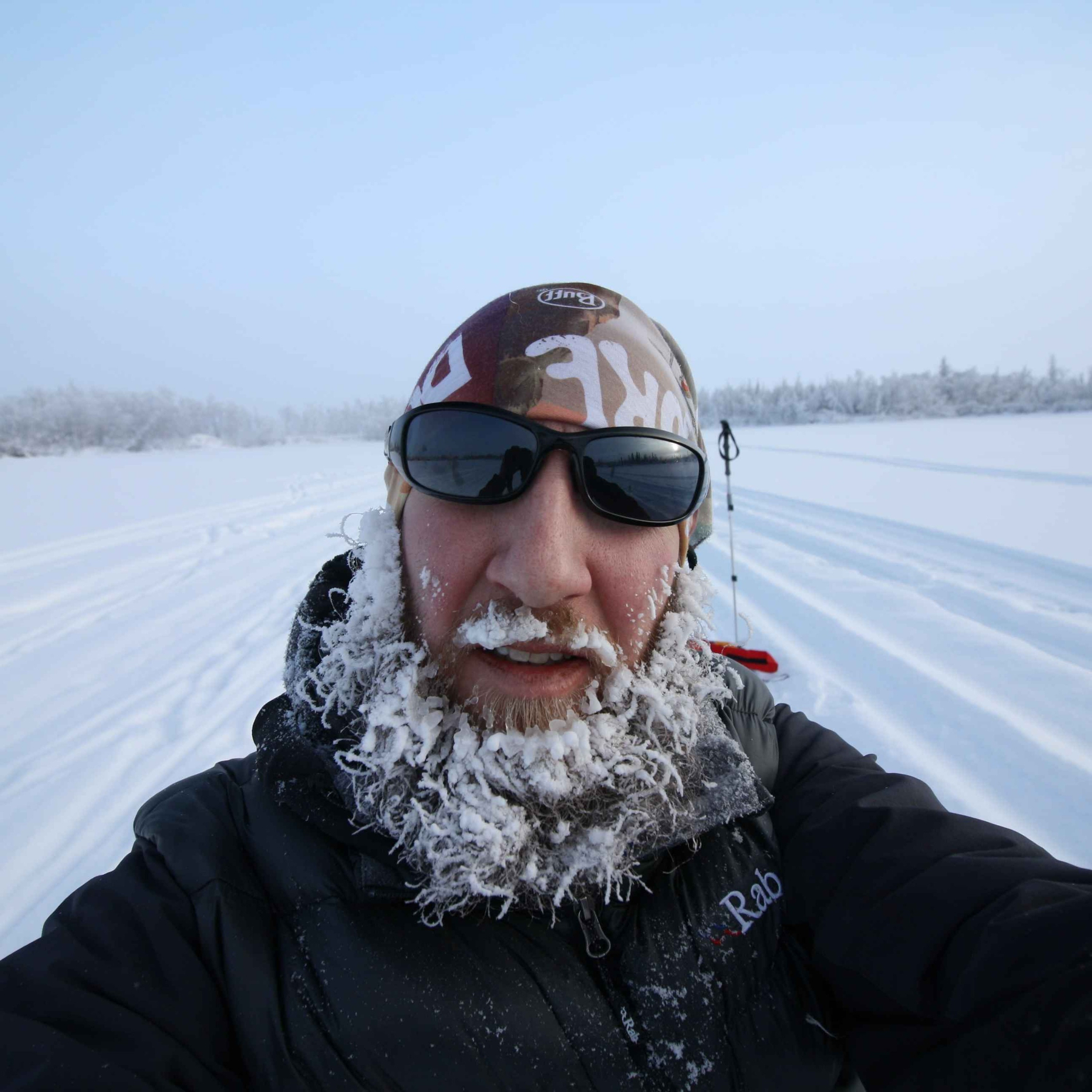 Auto-generated description: A person with a frosty beard and sunglasses is standing in a snowy landscape.