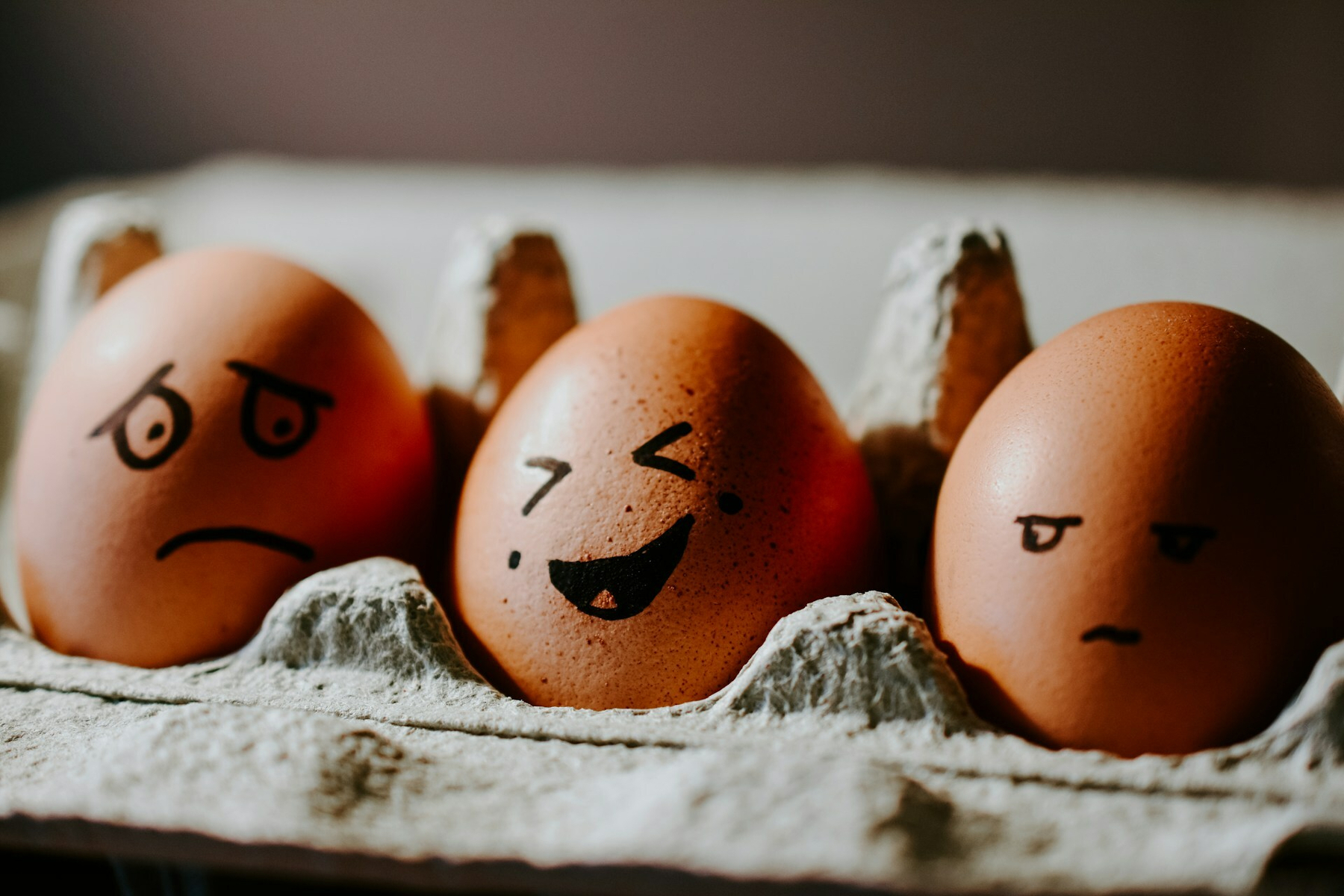 Auto-generated description: Three eggs in a carton have faces drawn on them, each showing different expressions.
