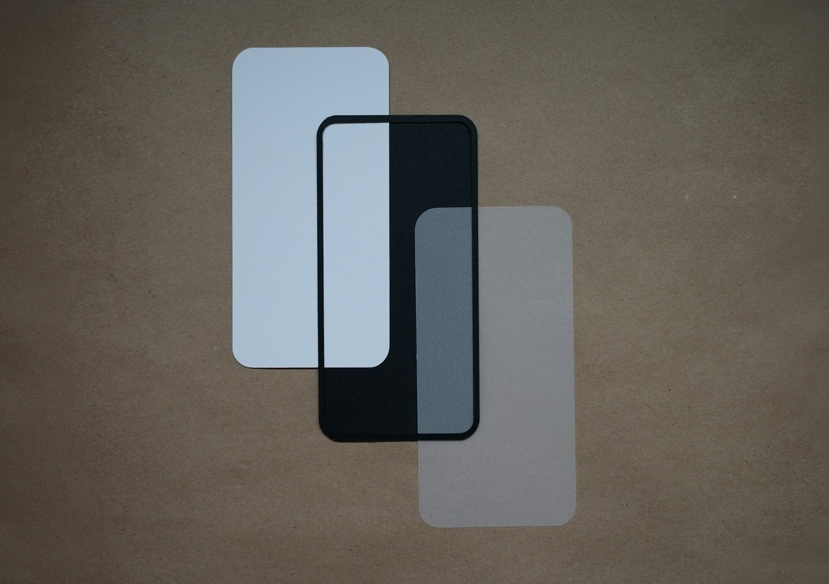 Three overlapping phone-shaped piece of glass in white, black, and translucent gray on a brown background.