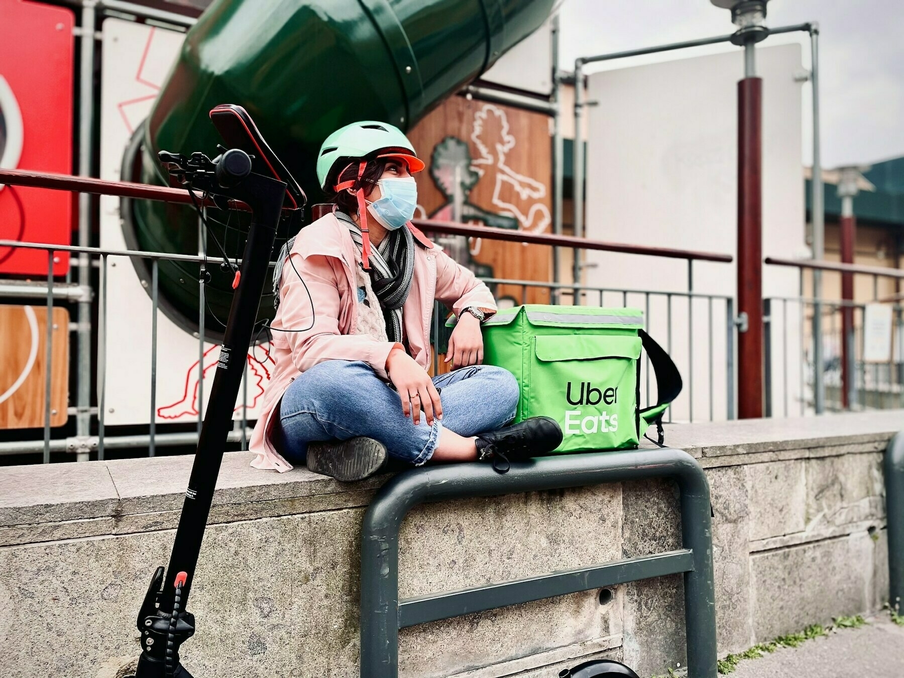 Man sitting on wall wearing a face mask with his arm resting on an Uber Eats delivery bag