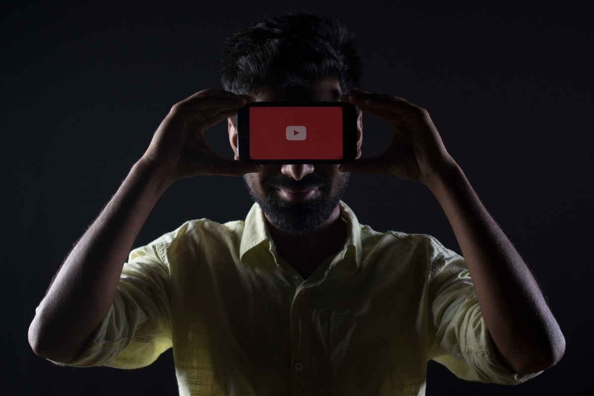 Silhouette of a person holding a smartphone with the YouTube logo in front of their face.