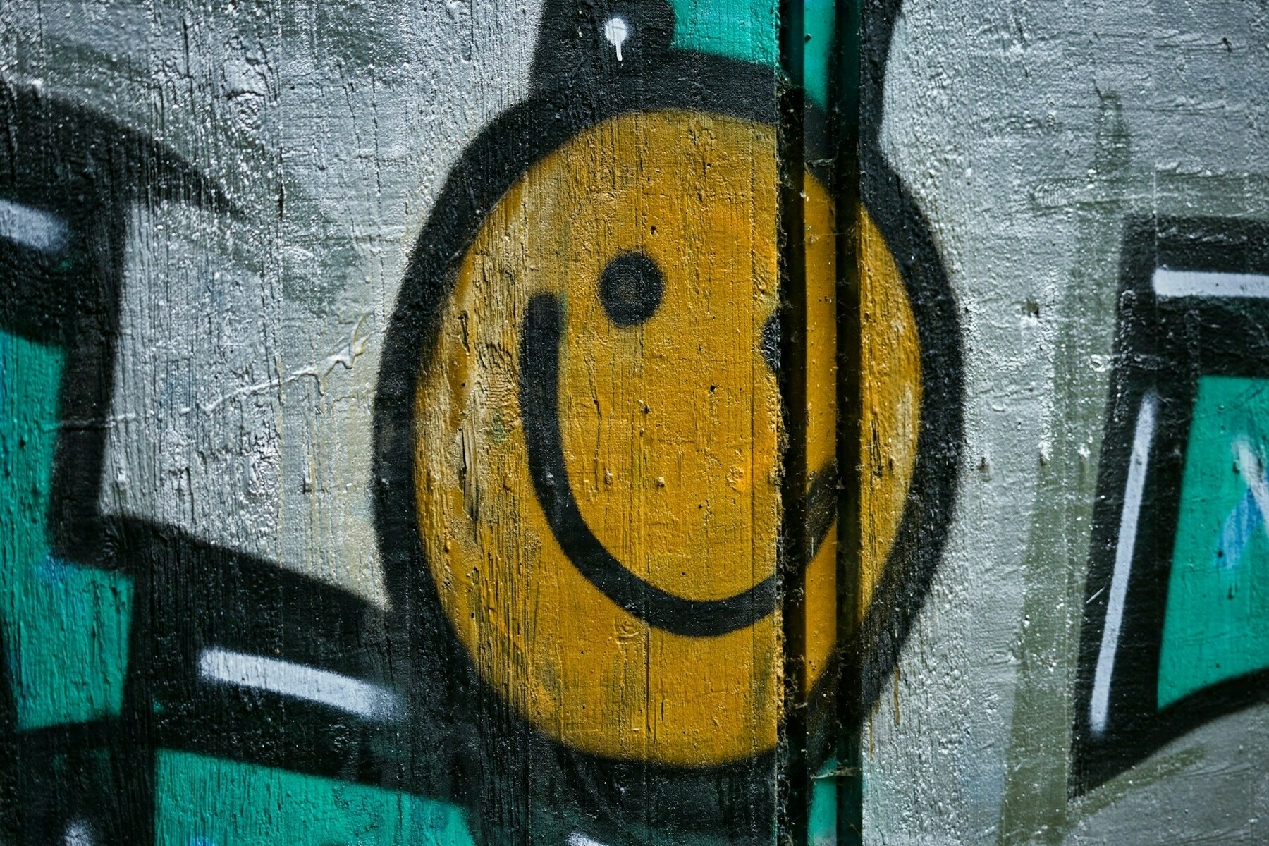 Auto-generated description: A yellow smiley face is painted on a textured wall with abstract graffiti elements in the background.