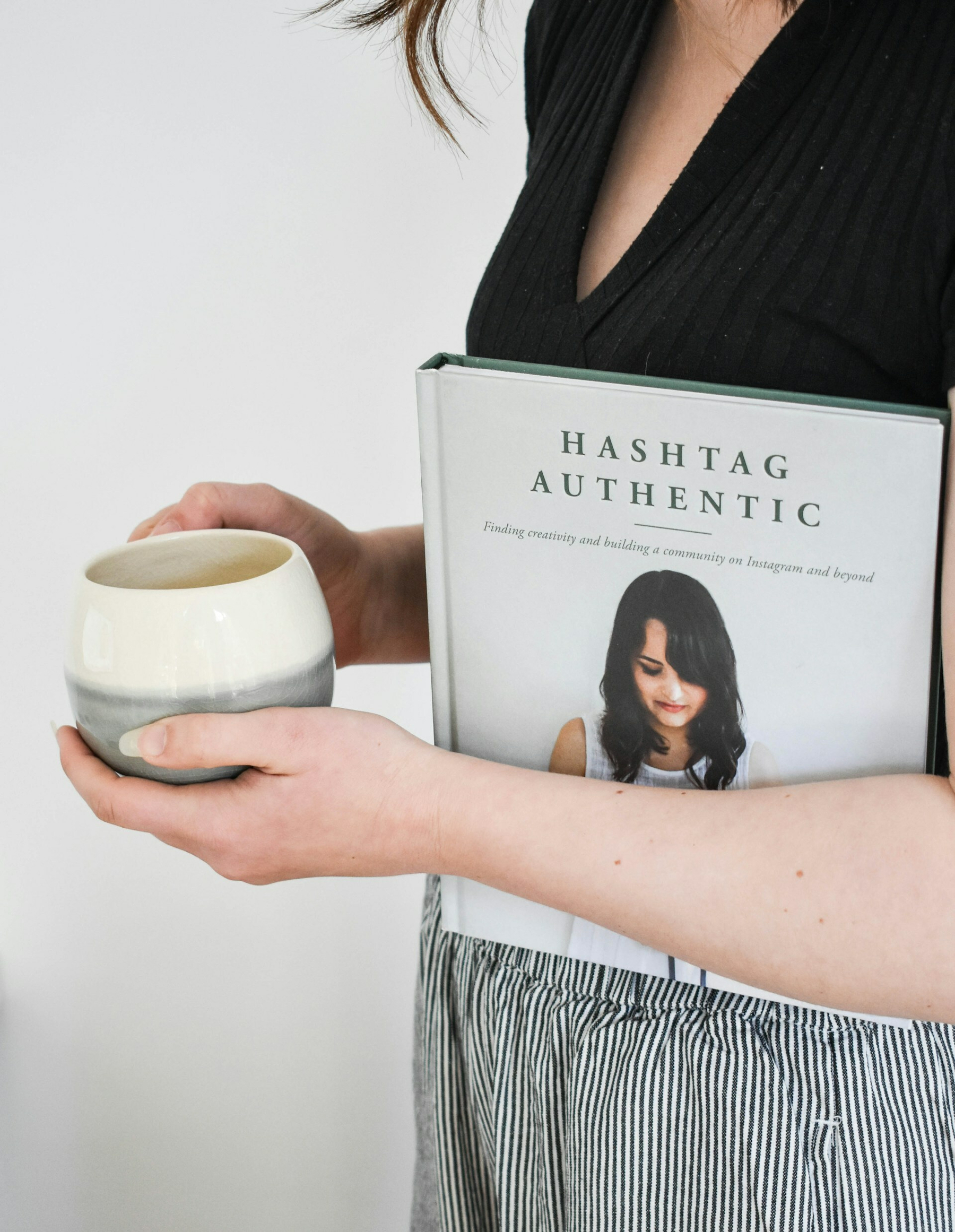 Auto-generated description: A person holds a book titled Hashtag Authentic and a cup.