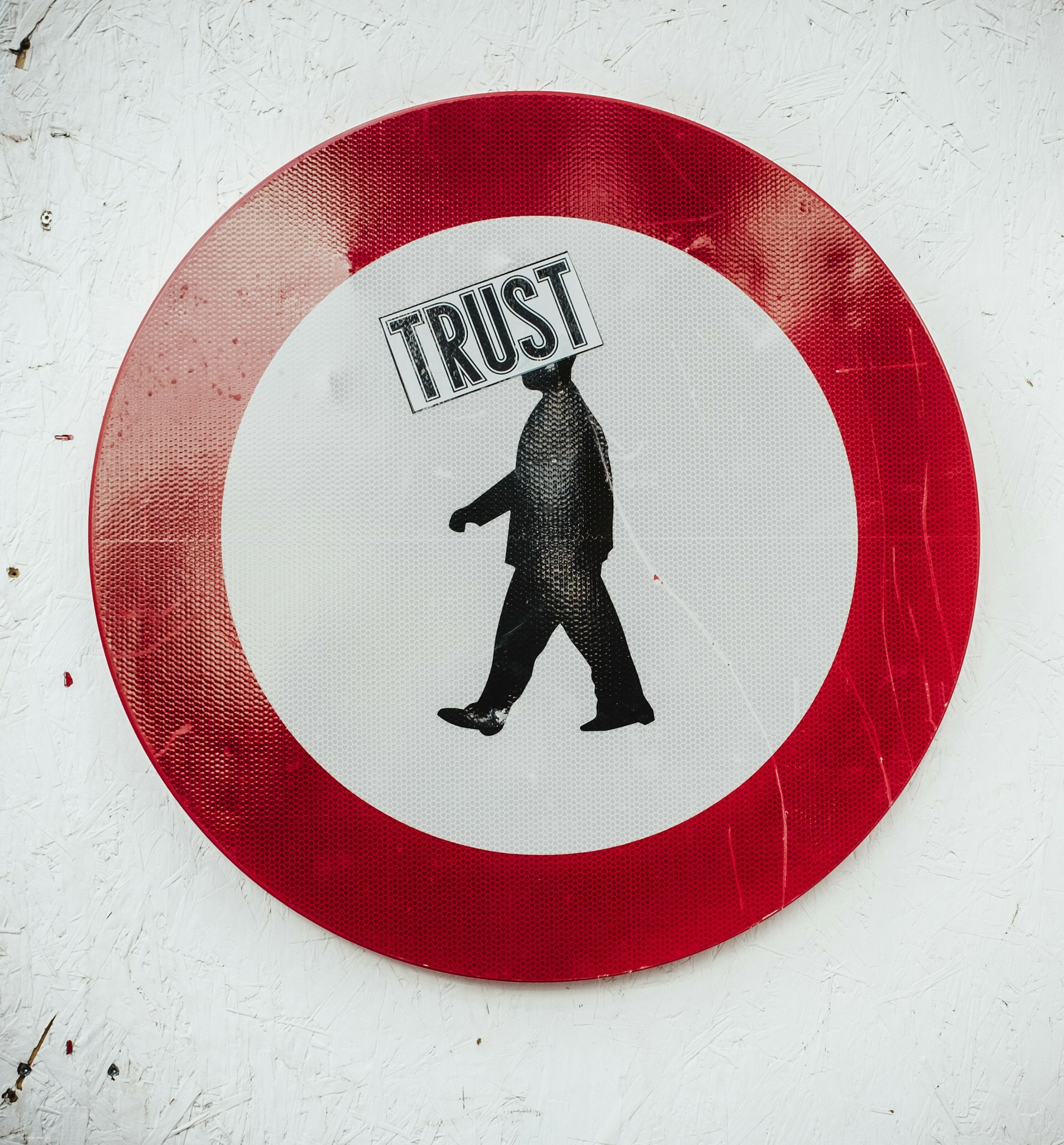 Auto-generated description: A circular sign with a red border depicts a silhouette of a walking person and the word TRUST above them.