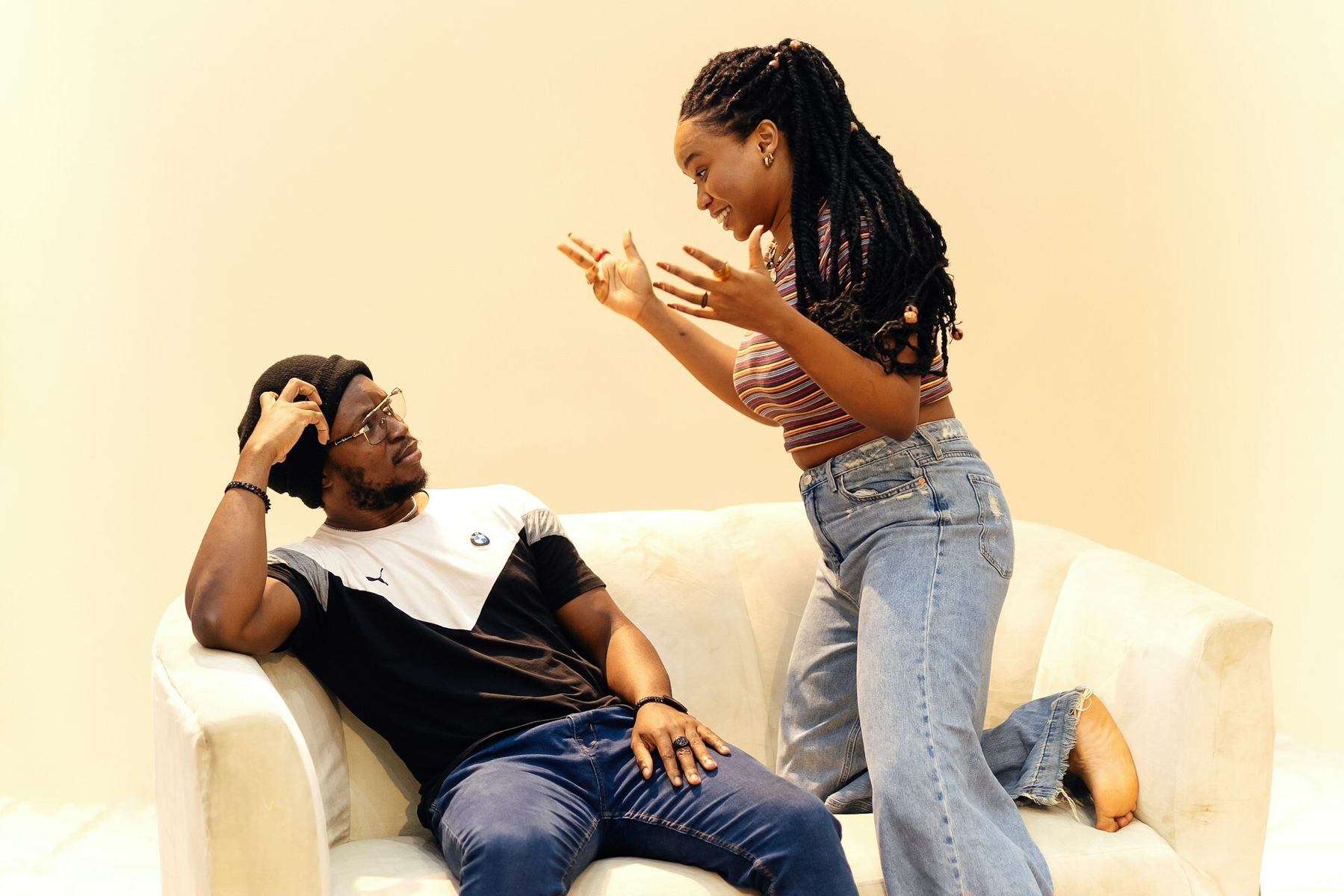 Auto-generated description: A woman passionately gestures while talking to a seated man on a white couch.