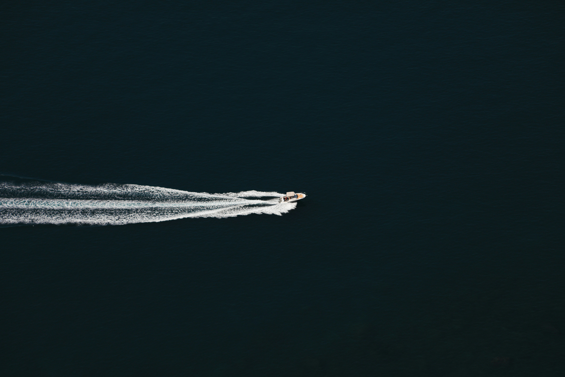 Auto-generated description: A boat is cruising across dark water, leaving a trail of white waves behind.