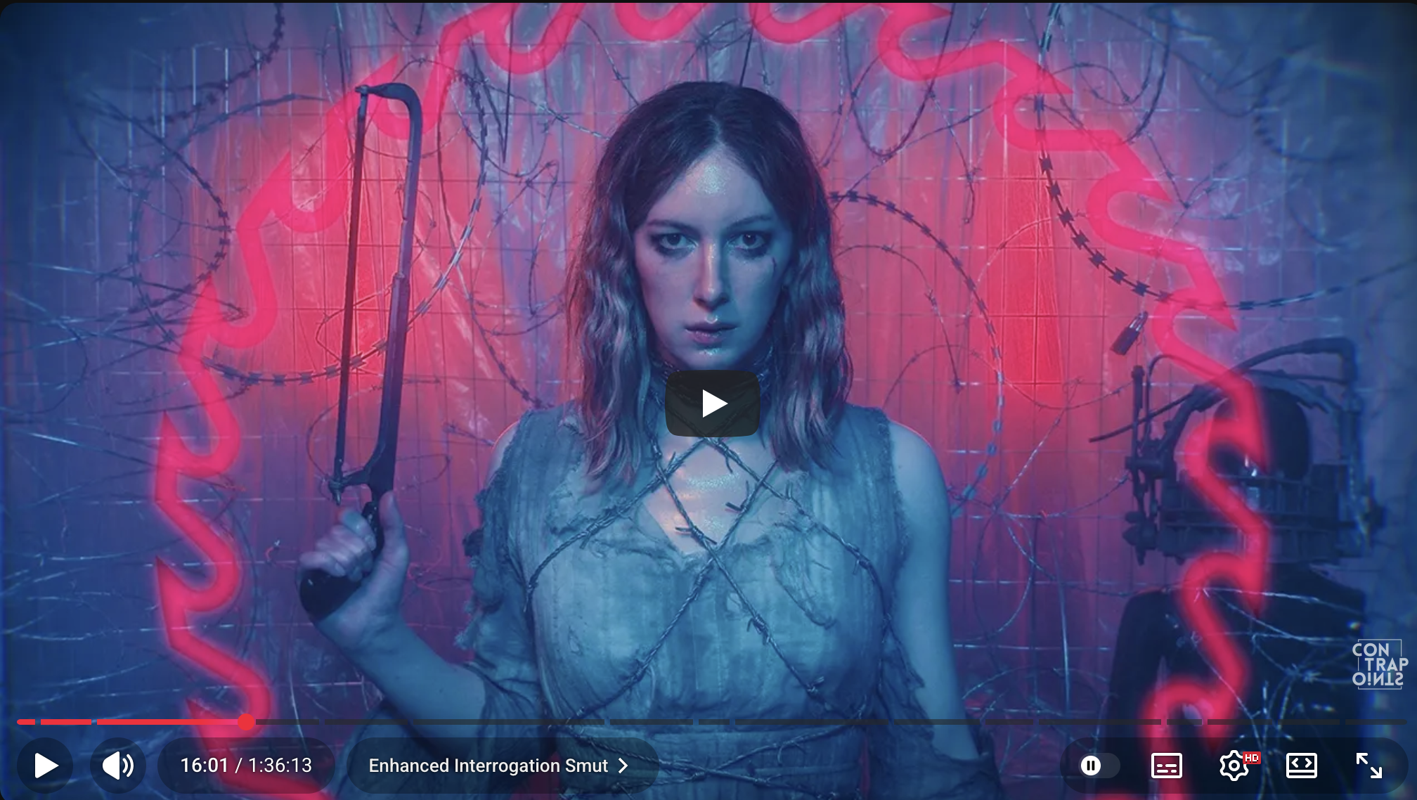 Auto-generated description: A person stands in front of a wire fence, illuminated by red and blue lighting, holding a whip-like object, creating a dramatic and intense atmosphere.