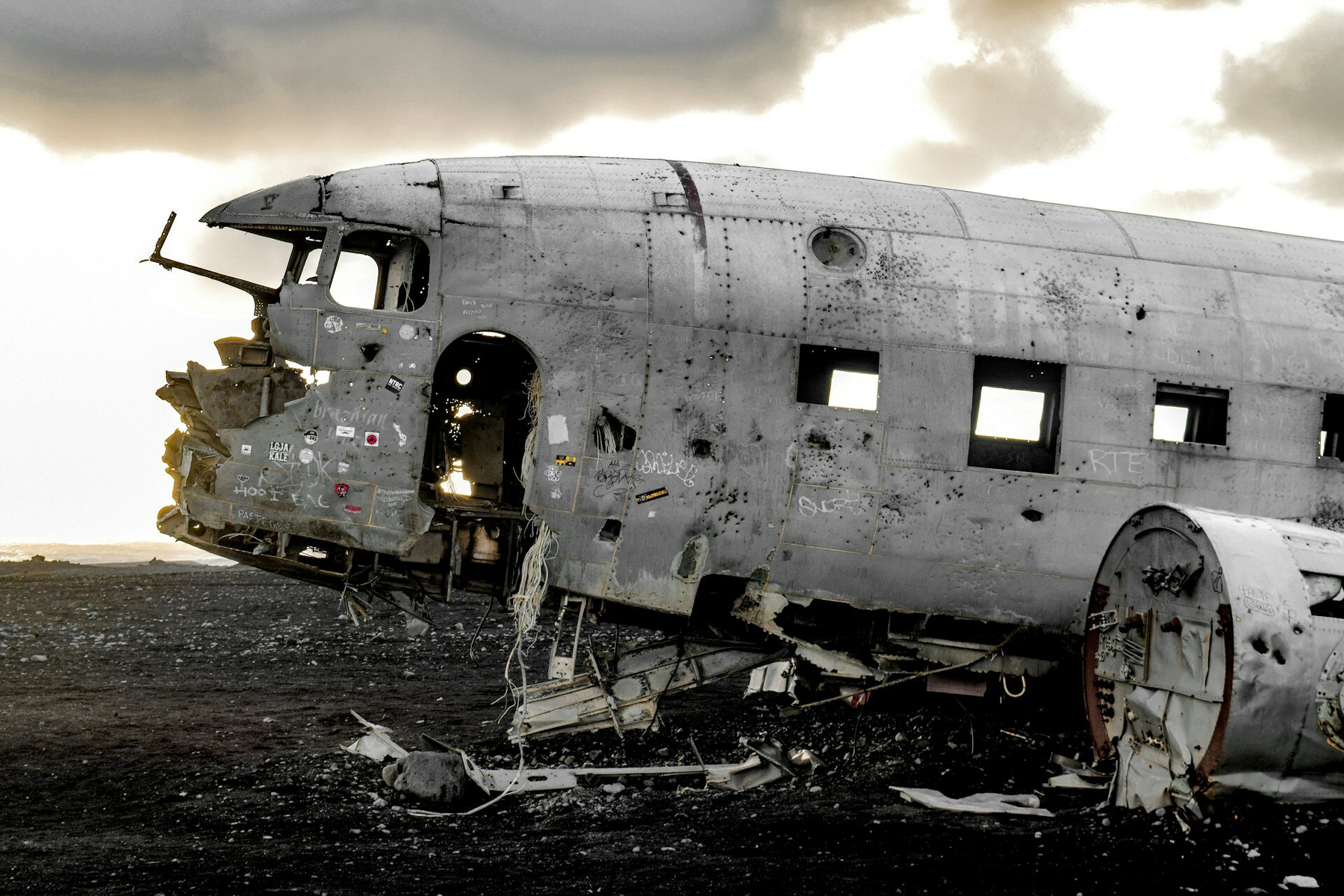Auto-generated description: A weathered, abandoned airplane wreck rests on a desolate terrain under a cloudy sky.