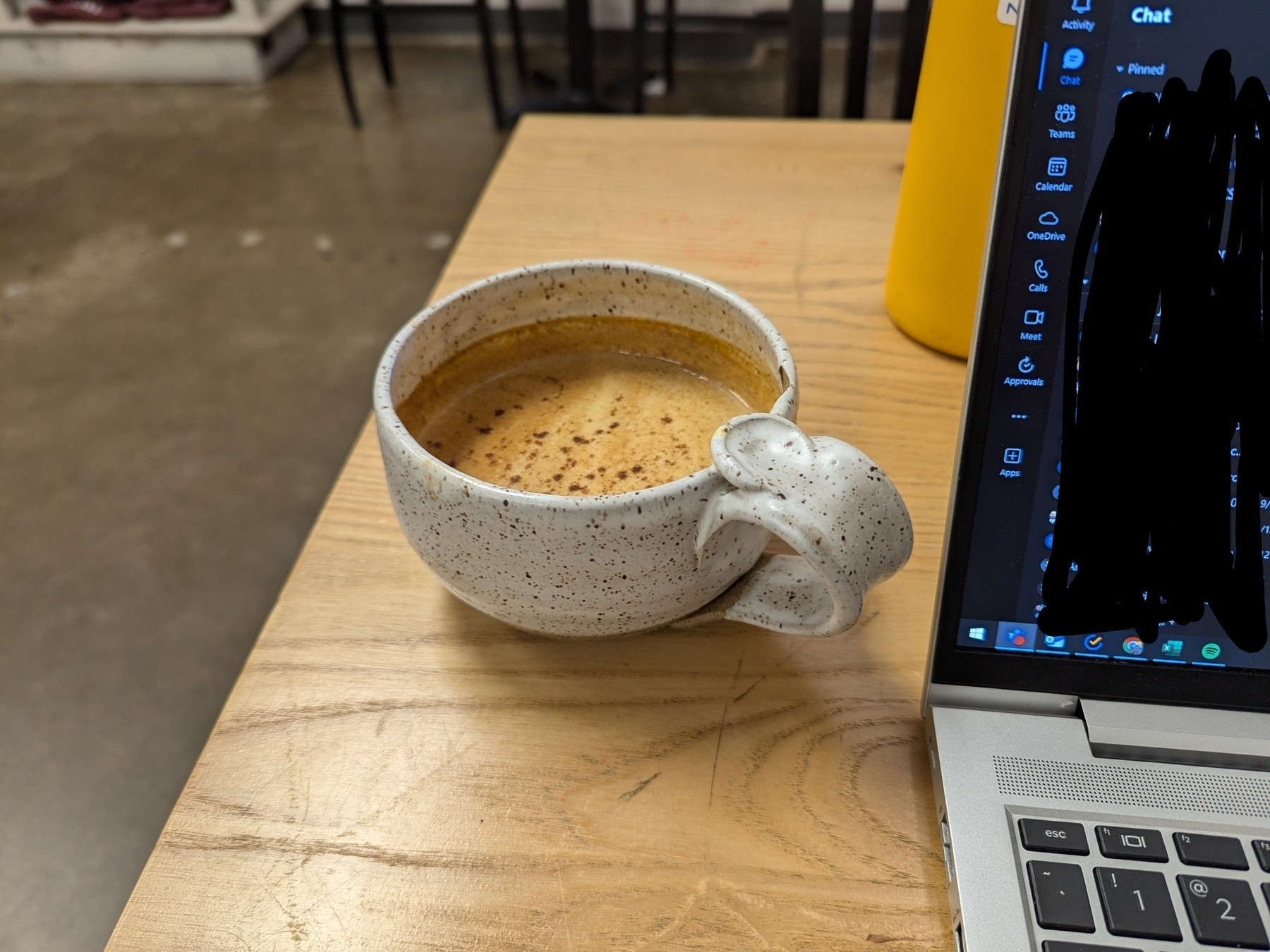 A coffee mug sitting on a wooden table with a laptop on the right edge of the frame.