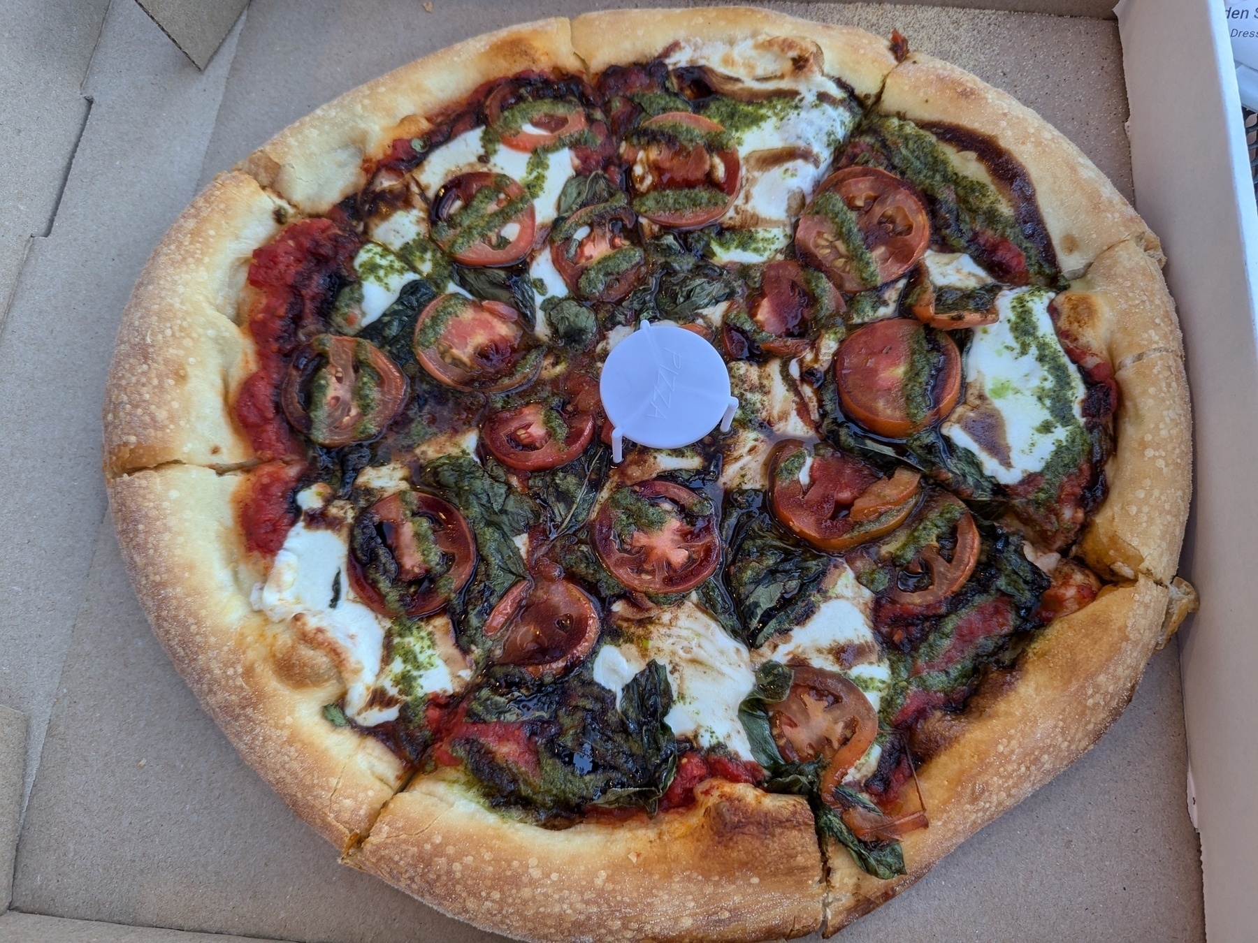 A margherita pizza drizzled in pesto and olive oil in a pizza box