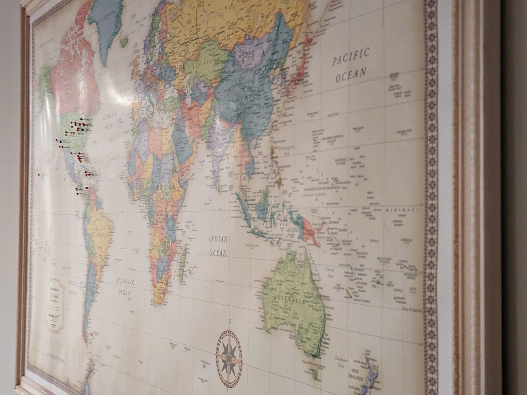 A framed world map on a wall with a handful of pins around north America.