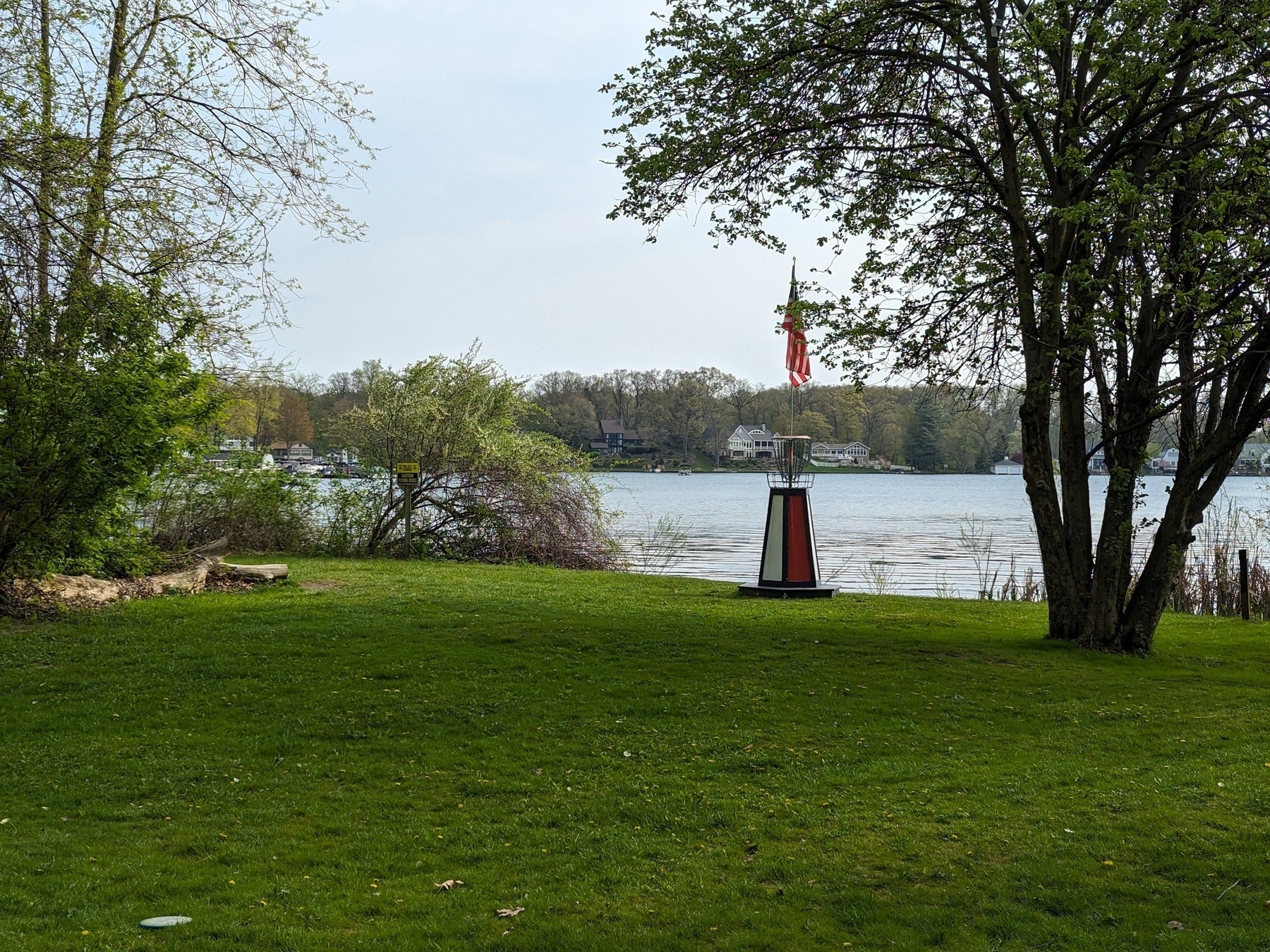 A disc golf basket raised on top of a mini lighthouse with a lake in the background.