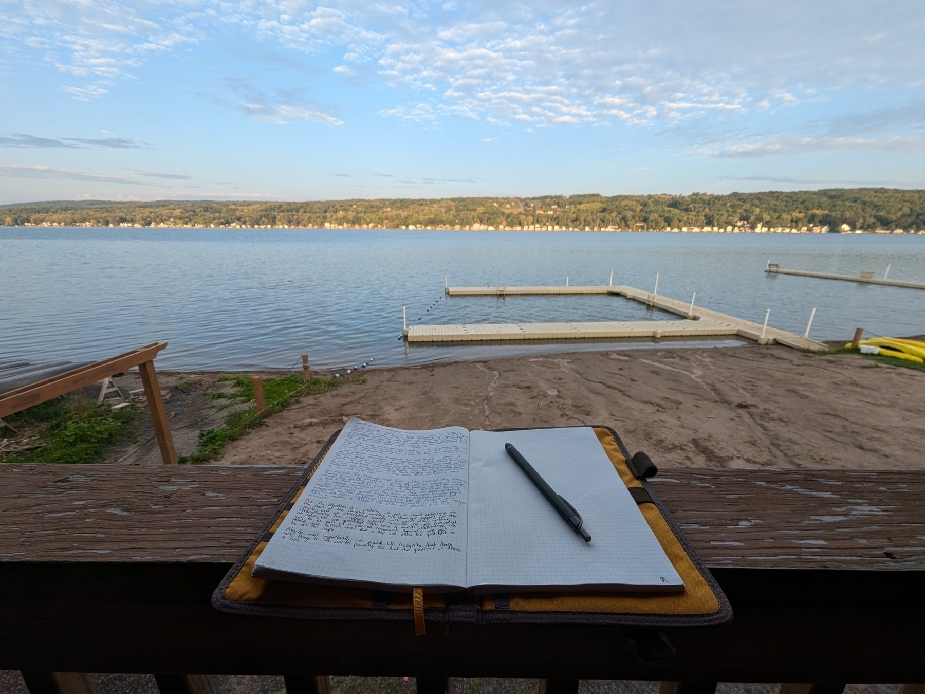 An open journal rests on a deck railing with a lake in the background.