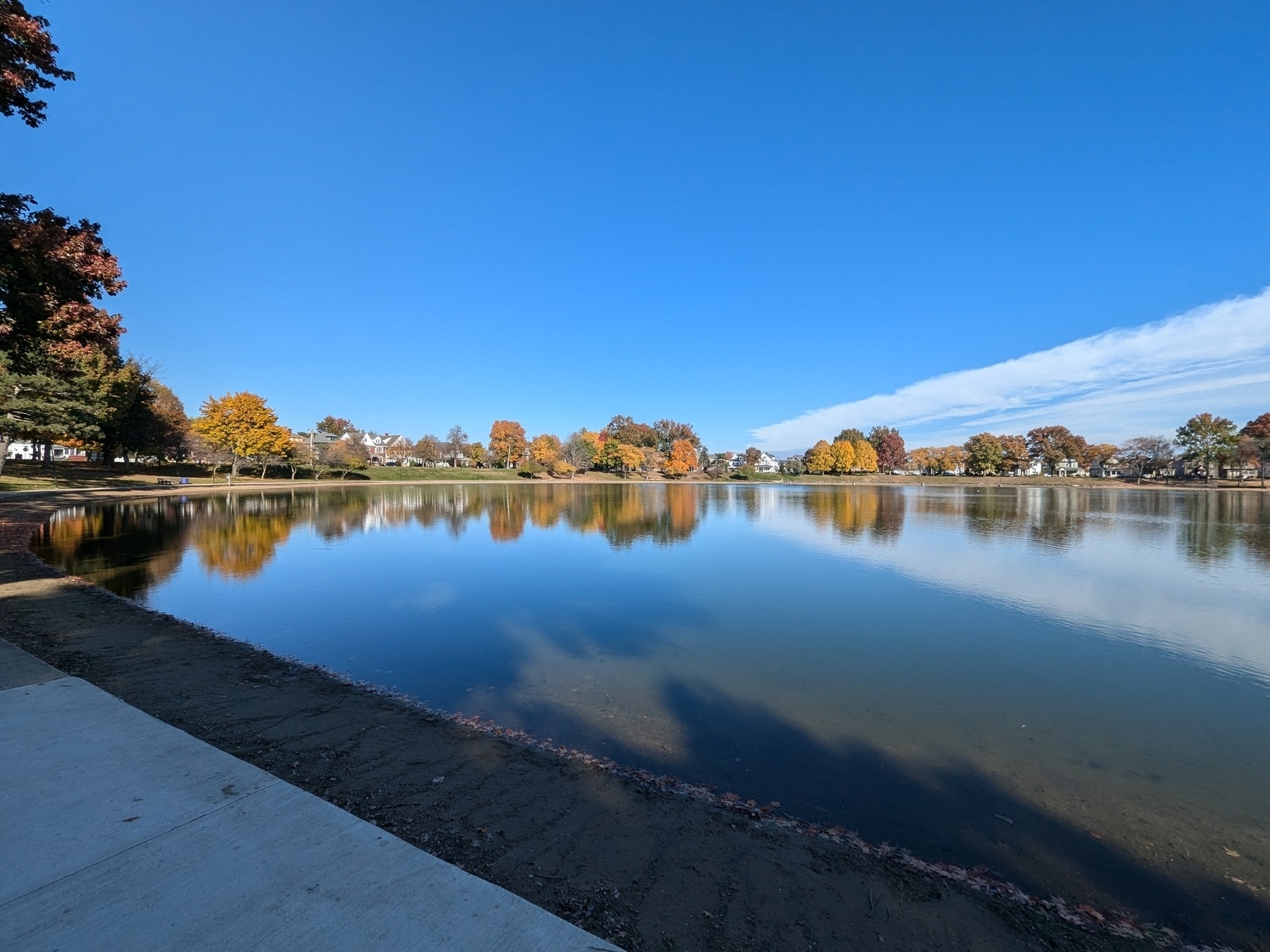 A serene lake reflects the clear blue sky and colorful autumn trees along its shoreline.